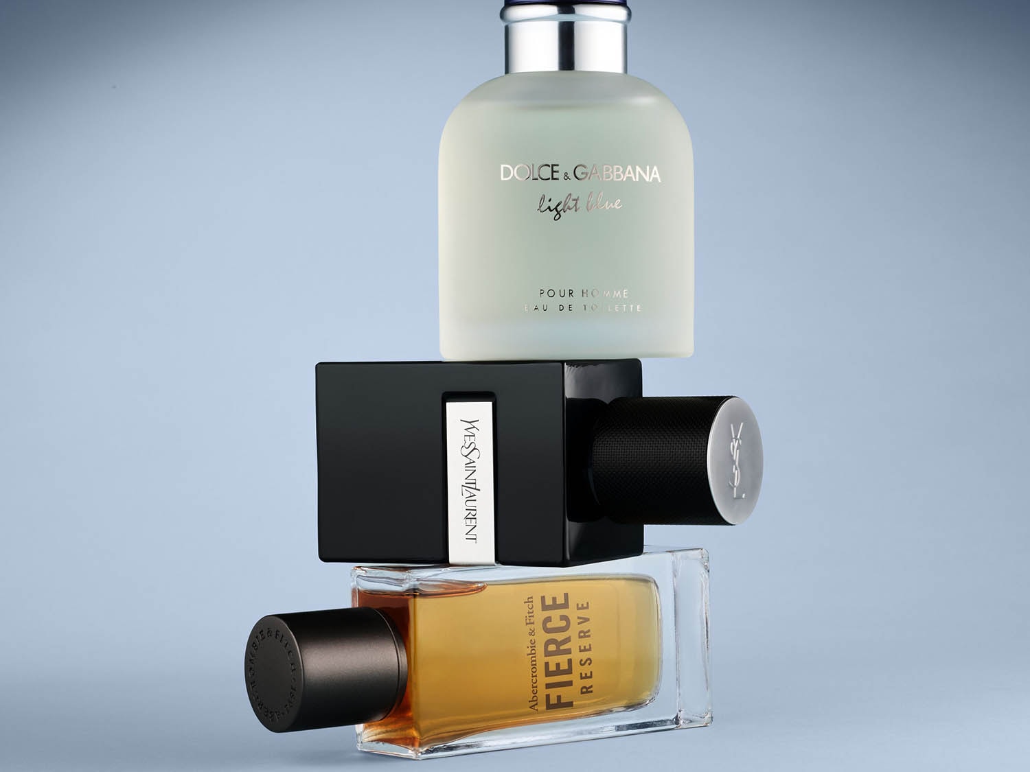 Tři flakony pánských parfémů různých značek naskládané na sobě: Dolce & Gabbana Light Blue, YSL a Abercrombie & Fitch Fierce Reserve.