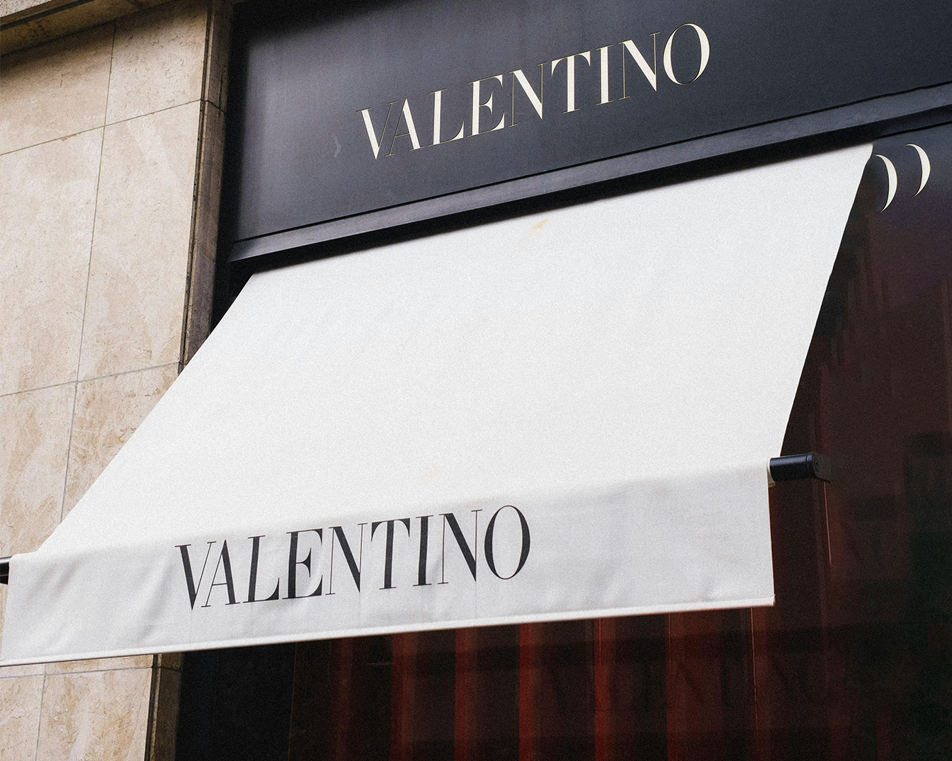 De gevel van een Valentino winkel met een witte luifel waarop de naam van het merk in zwarte letters staat, boven een zwarte achtergrond met de merknaam in gouden letters.
