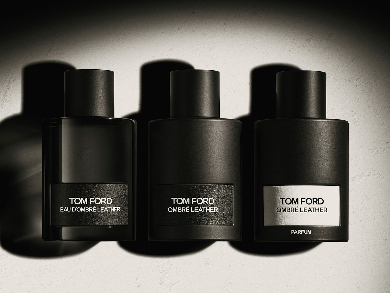 Trys Tom Ford Ombré Leather aromato buteliukai: Eau D'Ombré Leather, Ombré Leather ir Ombré Leather Parfum, visi juoduose matiniuose buteliukuose su etiketėmis.