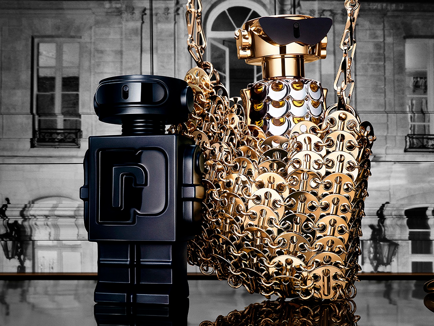 Zwei Parfümflaschen in Roboterform stehen vor einem Gebäude: eine schwarze und eine goldene, die mit einer goldenen Kette verziert ist.