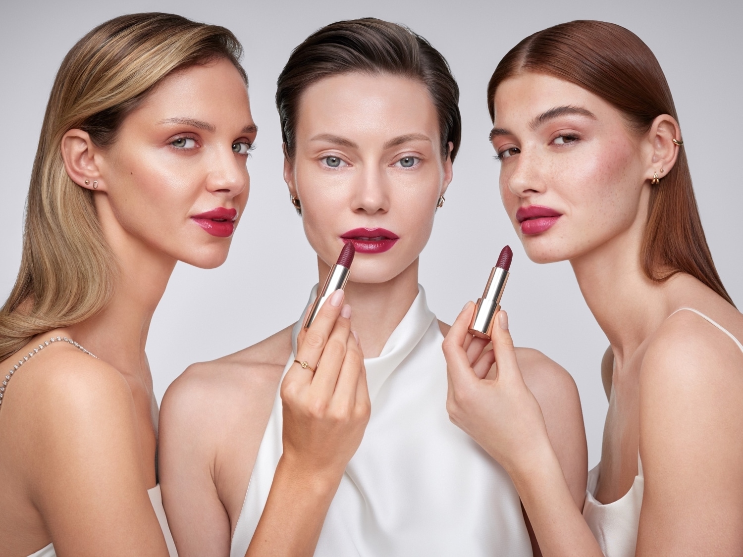 Trzy kobiety prezentują szminkę w złotym opakowaniu, każda z nich ma usta pomalowane na intensywny, ciemnoróżowy kolor.