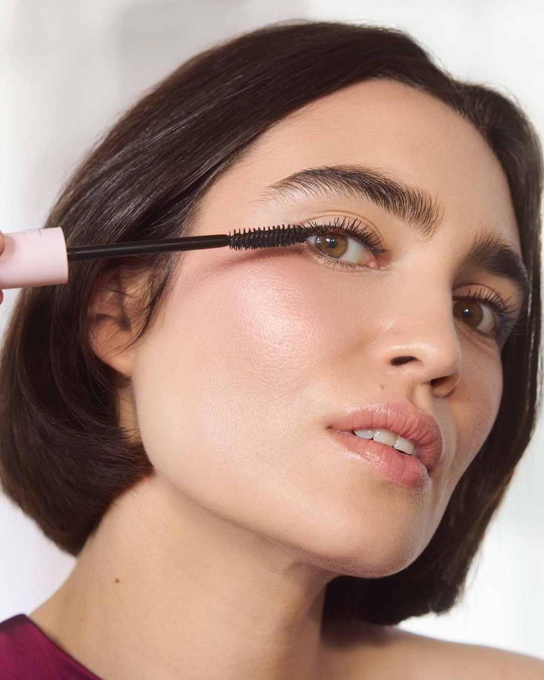 Nahaufnahme einer Frau, die mit einer schwarzen Bürste Mascara auf ihre Wimpern aufträgt, um einen strahlenden Augenaufschlag zu erzielen.