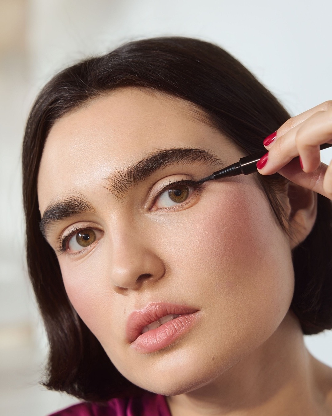Nahaufnahme einer Frau, die mit einem schwarzen Eyeliner einen Lidstrich zieht, um ihren Blick zu intensivieren.