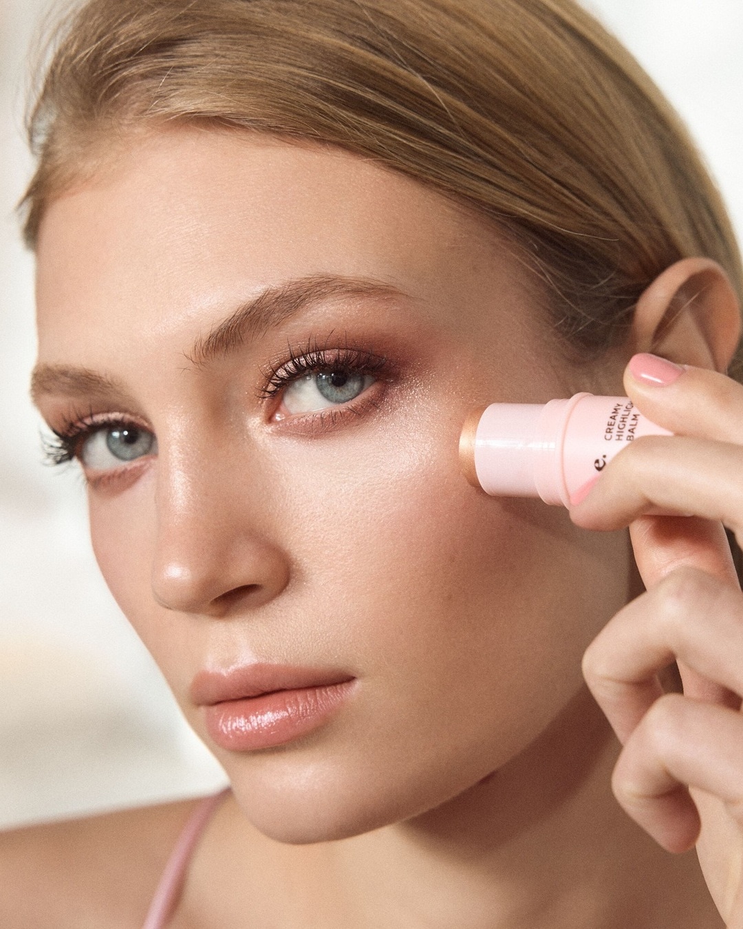 Nahaufnahme einer Frau, die einen cremigen Highlighting-Balsam-Stick auf ihre Wange aufträgt, um einen strahlenden Glanz zu erzielen.