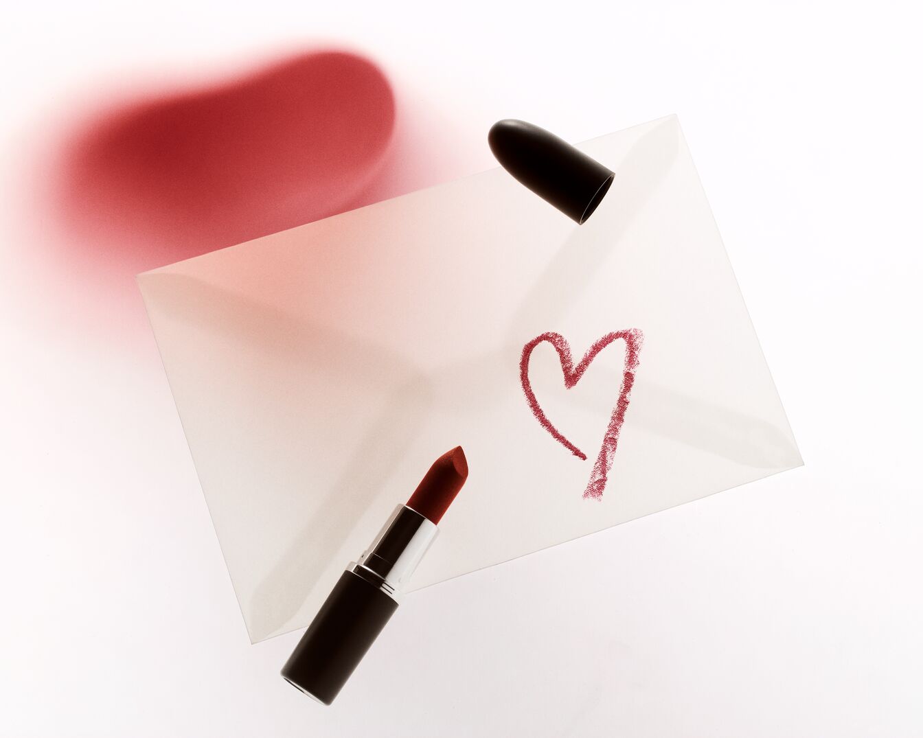 Egy piros rúzs egy borítékon fekszik, amelyre egy piros szív van rajzolva, a szerelem és a szépség üzenetét sugallva.