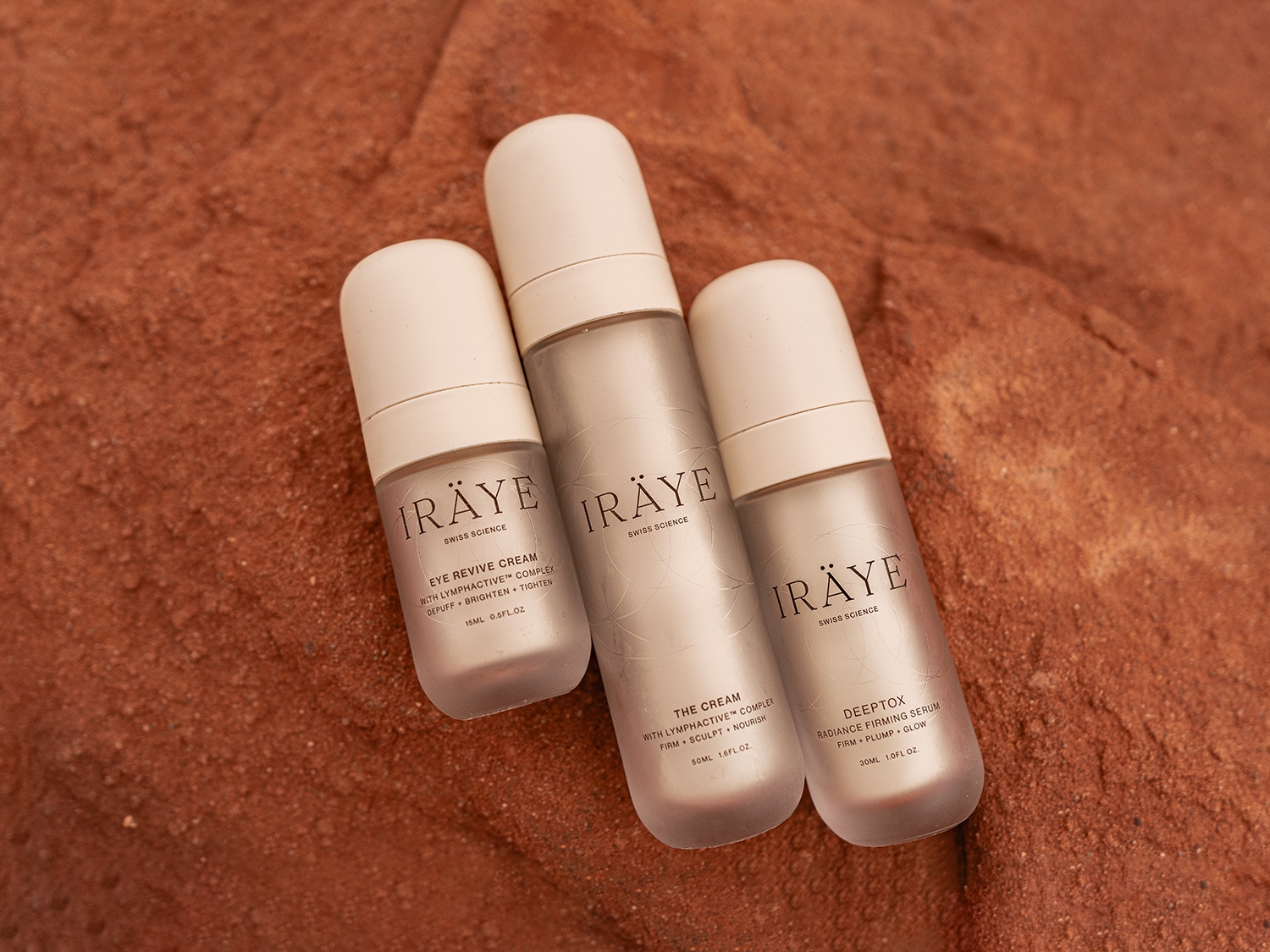 Découvrez la collection IRÄYE Swiss Science : Crème Yeux Revive, Crème et Sérum Raffermissant Éclat Détoxt, présentés dans des flacons élégants sur un fond texturé.