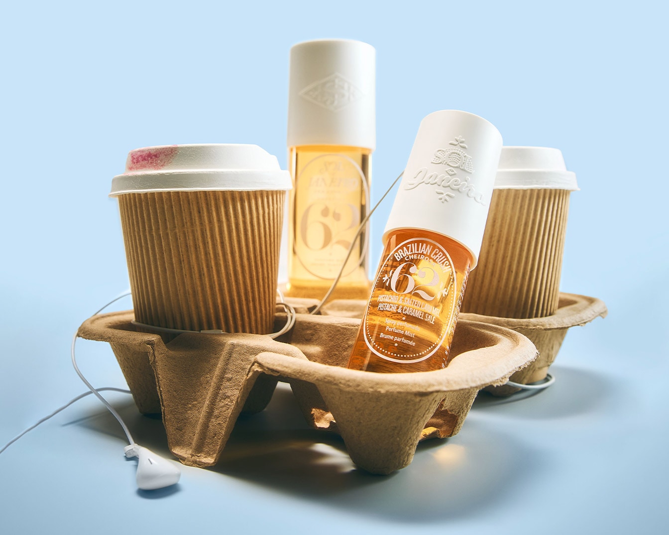 Découvrez le parfum Brazilian Crush Cheiros '62 de Sol de Janeiro, un mélange ensoleillé de pistache et de caramel salé, présenté dans un flacon ambré à côté de gobelets à café.