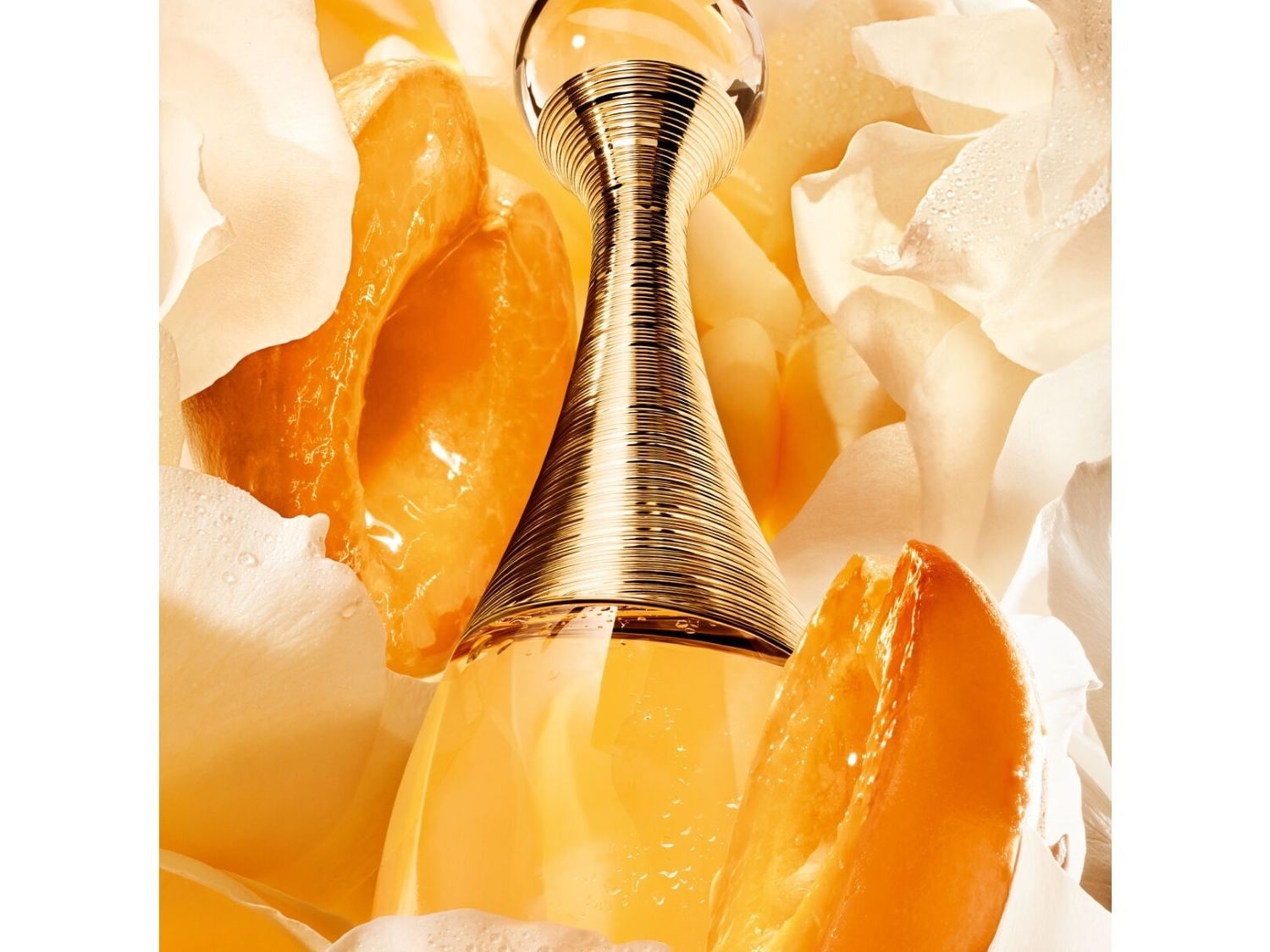 Découvrez le parfum J'Adore dans son flacon doré emblématique, entouré de pétales de fleurs blanches et de tranches d'orange juteuses.