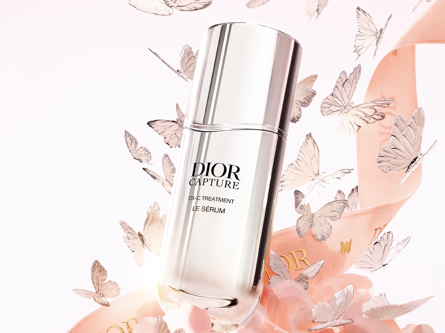 Dior Capture OX-C Treatment Le Sérum in een heldere fles met zilveren dop, omringd door zilveren vlinders en een roze lint.
