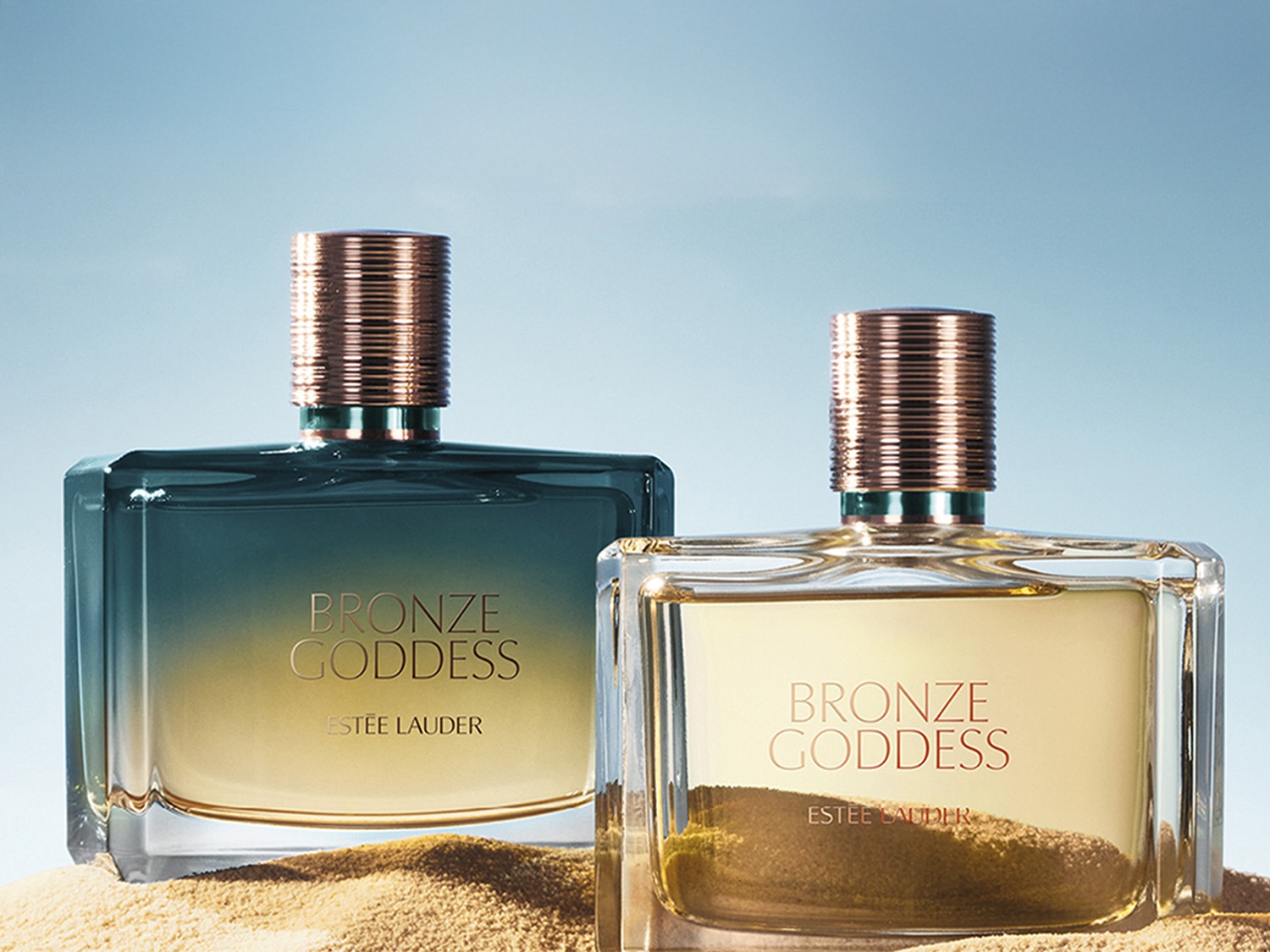 Deux bouteilles de parfum Bronze Goddess d'Estée Lauder, l'une avec un dégradé bleu-or et l'autre transparente avec des sédiments dorés, évoquant le luxe et la chaleur.