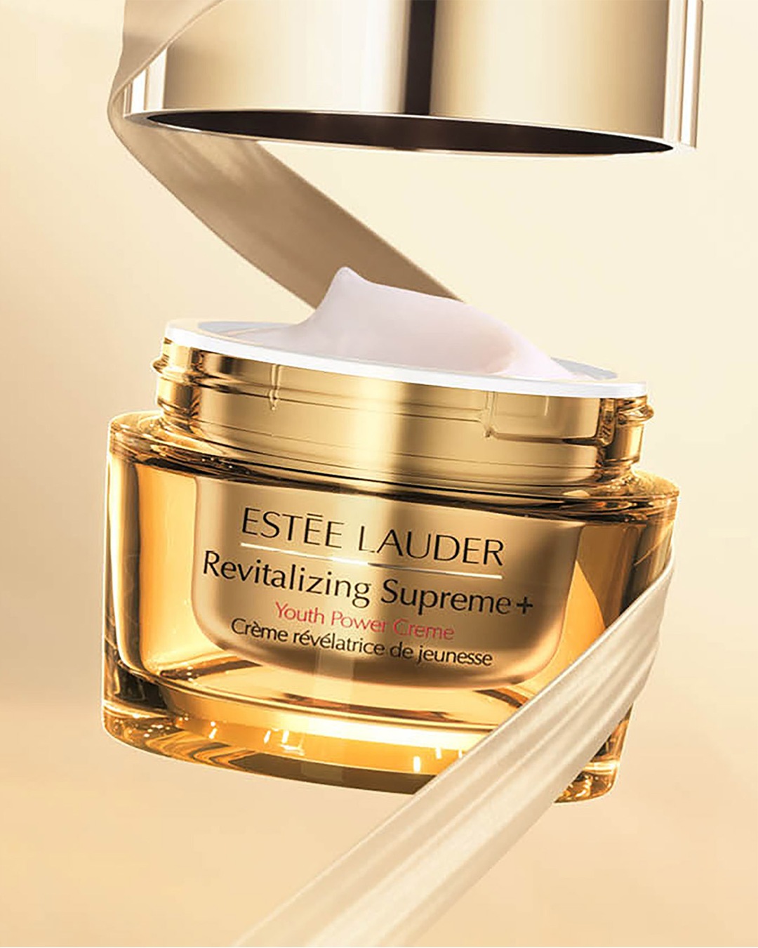 Découvrez la Crème Révélatrice de Jeunesse Revitalizing Supreme+ d'Estée Lauder dans son élégant pot doré, promesse d'une peau visiblement plus jeune et éclatante.
