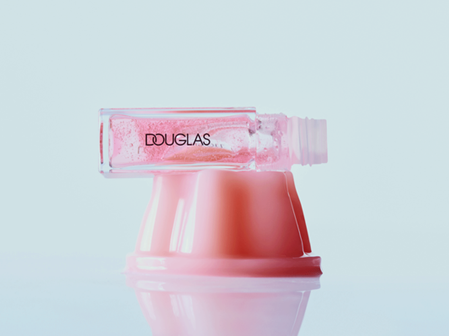 Das Douglas Nagelöl präsentiert sich in einer klaren, quaderförmigen Flasche mit rosafarbenem Inhalt, der auf einem rosa Sockel steht.