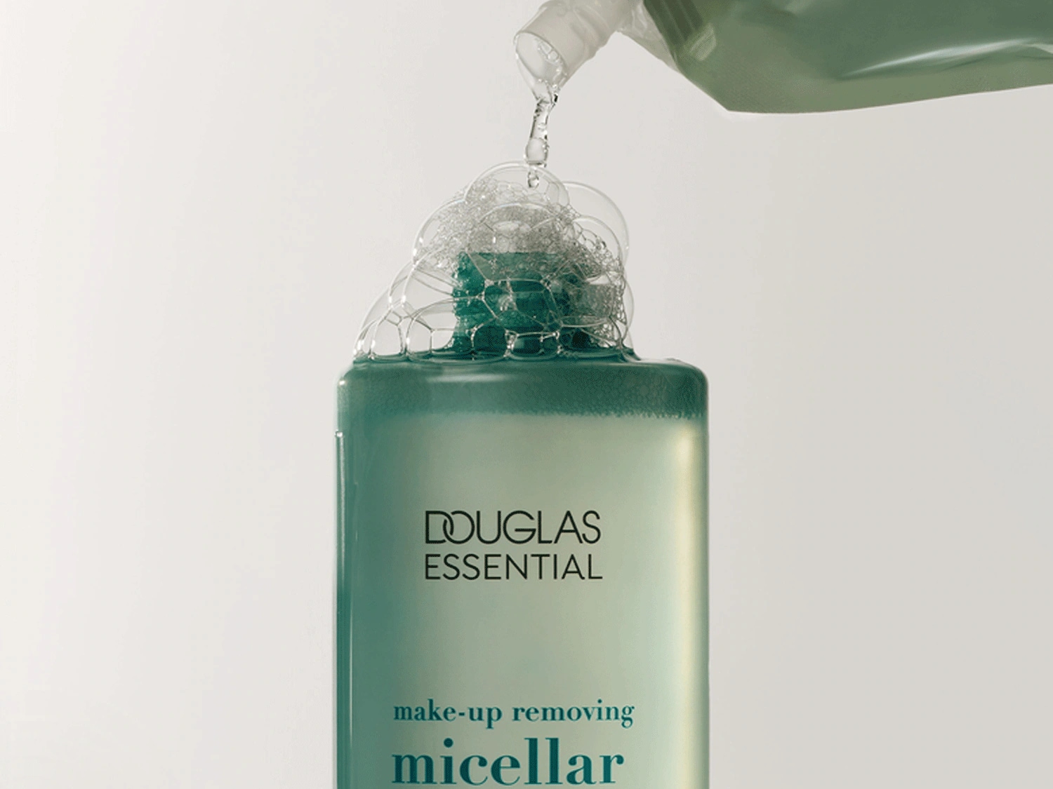 Klares Mizellenwasser wird in eine hellgrüne, rechteckige Flasche von Douglas Essential gegossen, die mit Schaum überläuft.