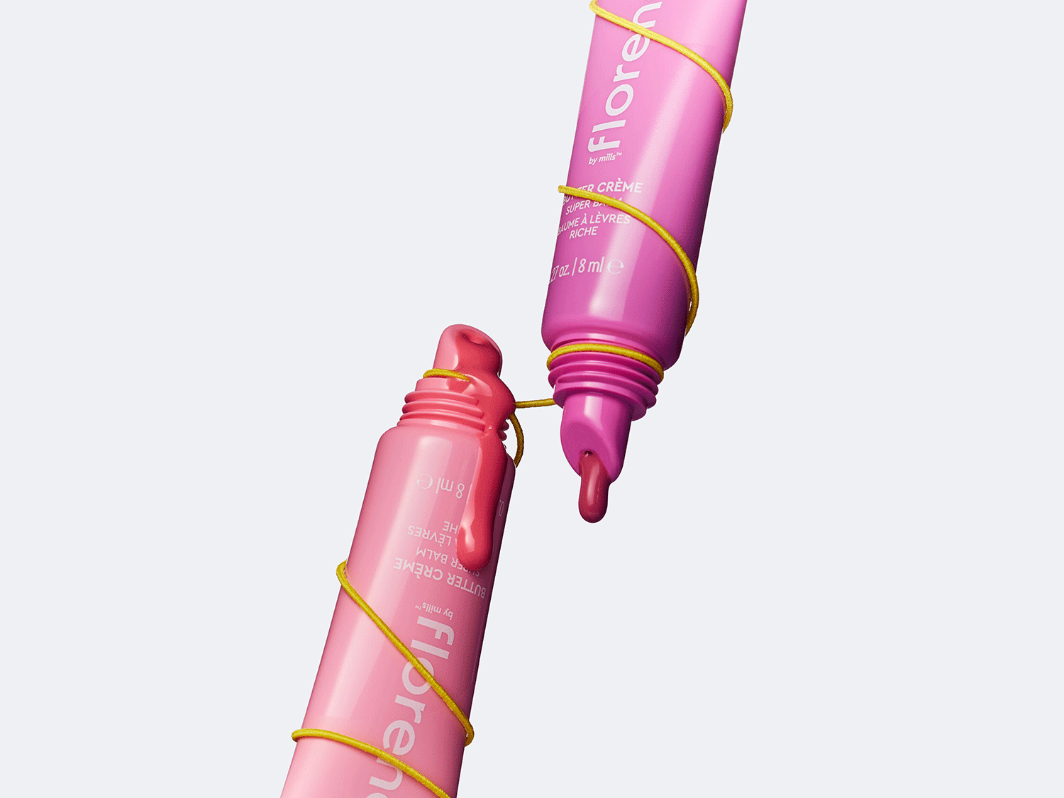Zwei rosa Lipgloss-Tuben von Florence by Mills, mit gelbem Faden umwickelt, zeigen die cremige Textur des Produkts.