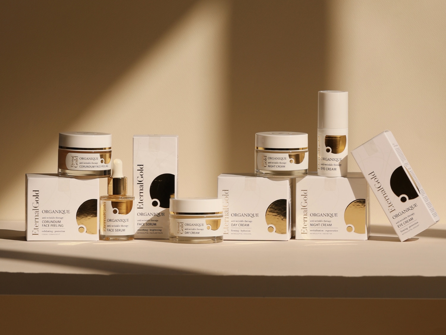 Złoty krem do peelingu twarzy Eternal Gold anti-wrinkle therapy CORUNDUM oraz serum do twarzy w szklanej butelce z pipetą na rozmytym tle.