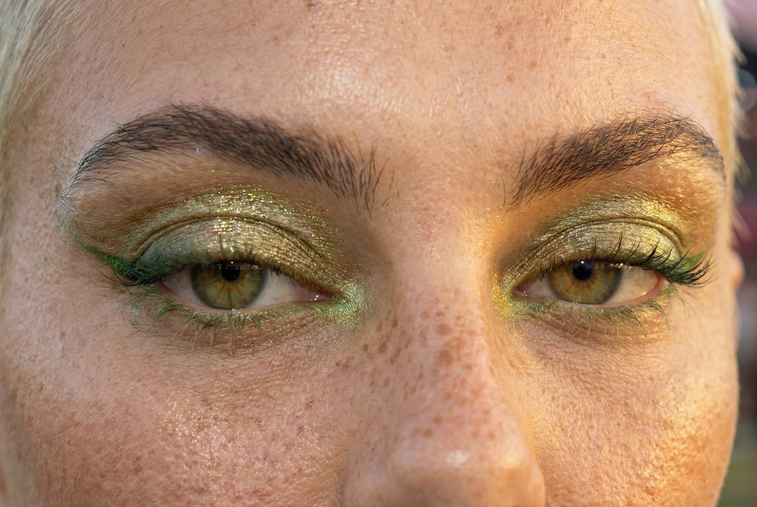 Nahaufnahme von Augen mit schimmerndem, grünem Lidschatten und passender grüner Wimperntusche für einen auffälligen Look.