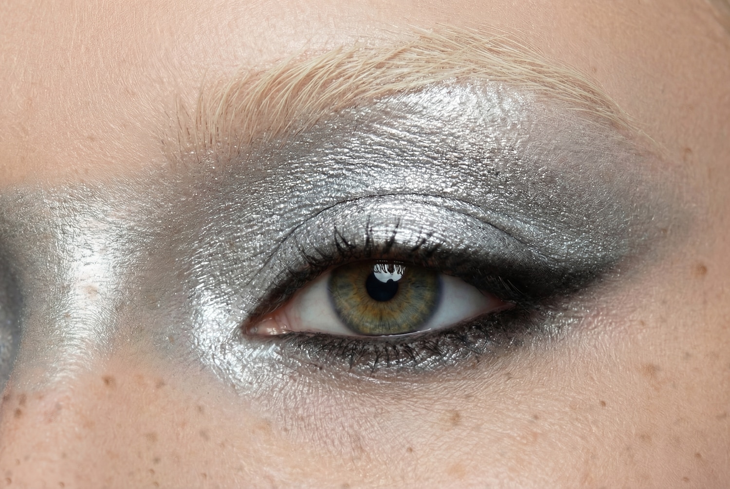 Nahaufnahme eines Auges mit silbernem Lidschatten, der bis zur Augenbraue reicht, und einem Hauch von schwarzem Eyeliner am oberen Lid.