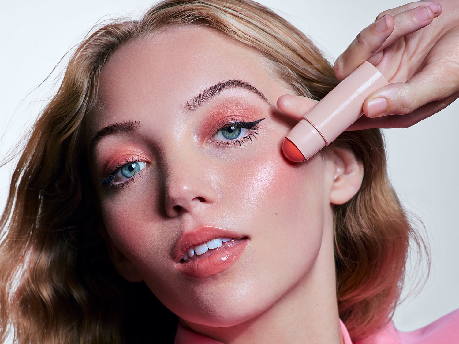 Nahaufnahme einer Frau, die einen Rouge-Stick auf ihre Wange aufträgt, um einen frischen und strahlenden Look zu erzielen.