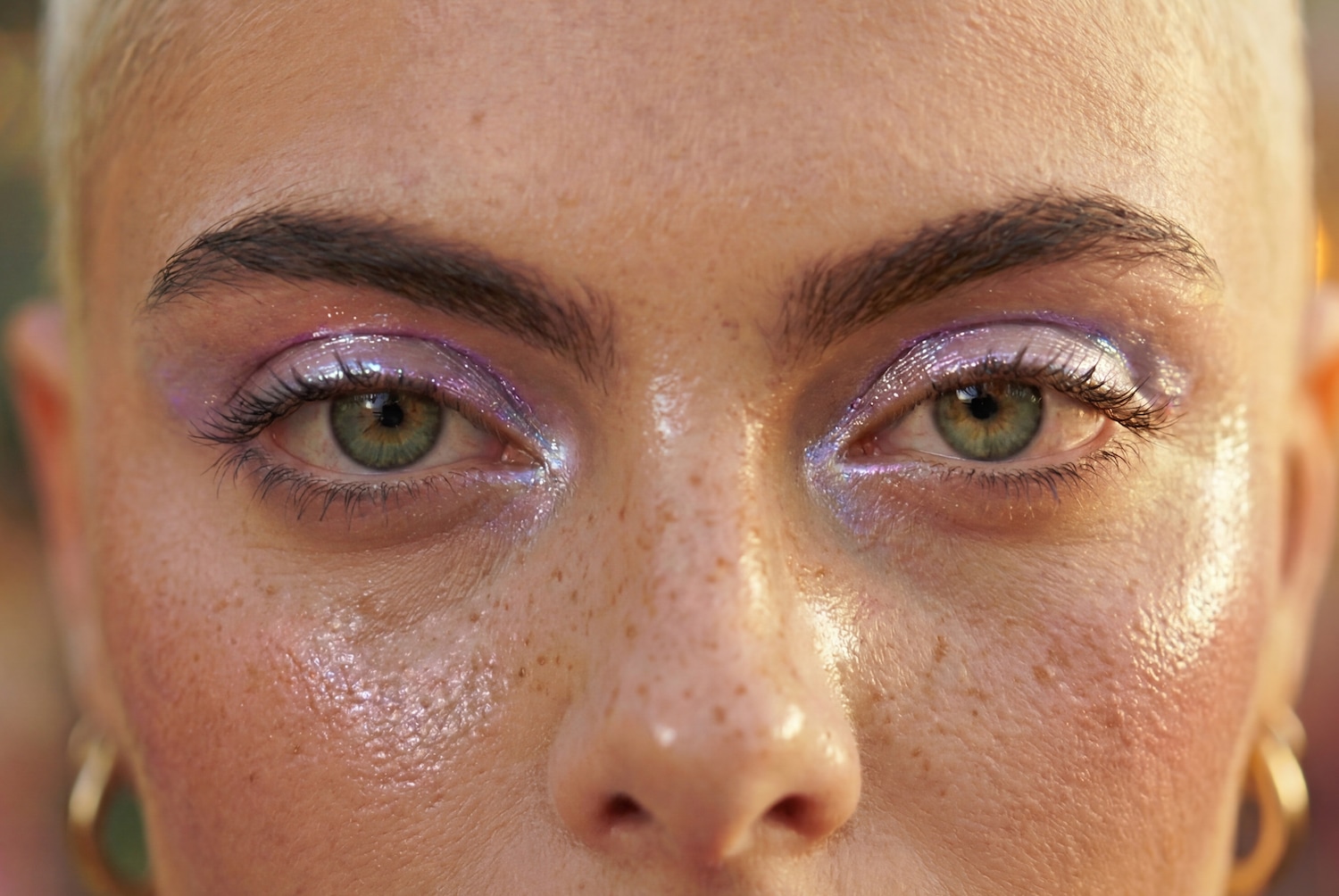Nahaufnahme eines Gesichts mit schimmerndem lila und silbernem Lidschatten, der die grünen Augen betont und einen strahlenden Look erzeugt.