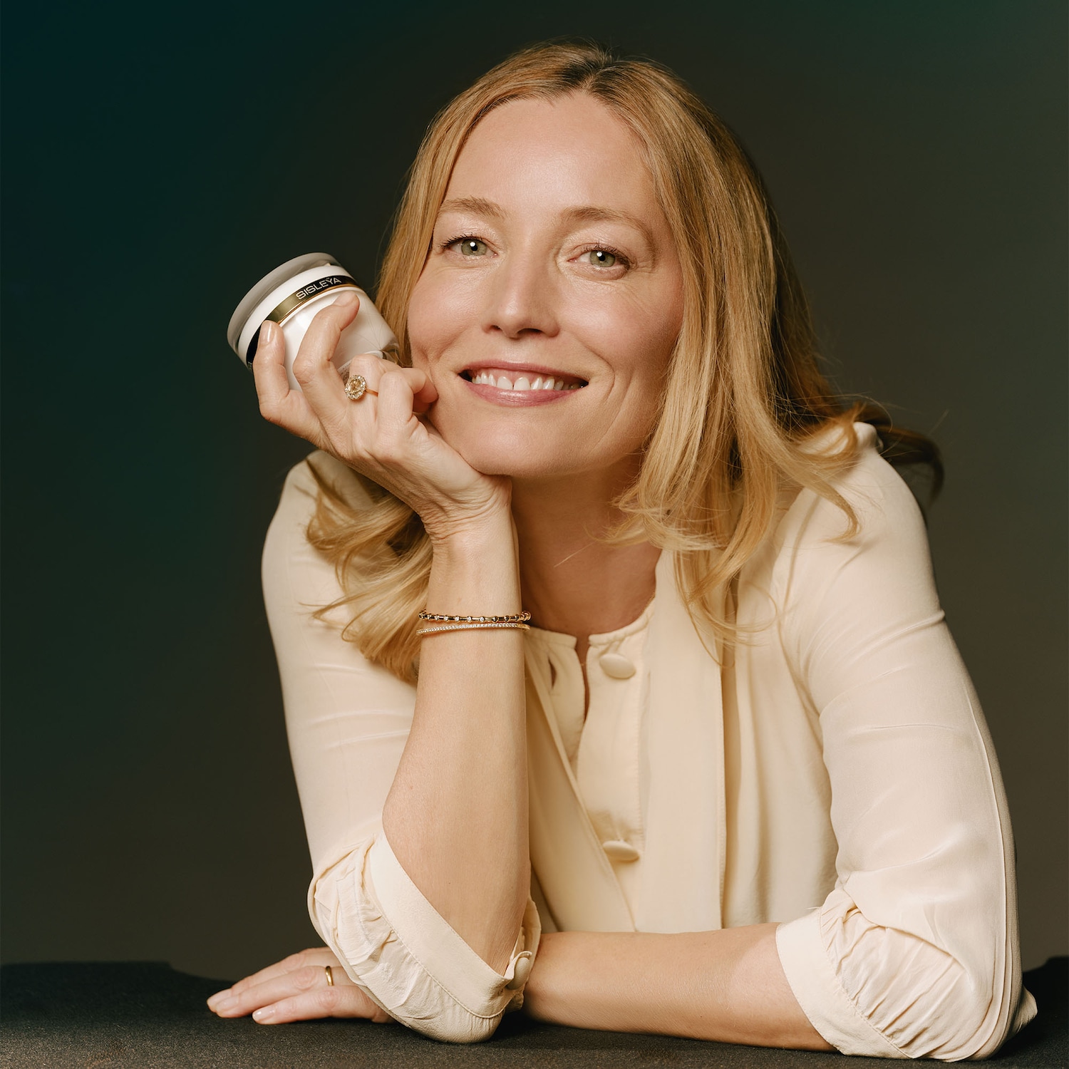 Une femme souriante tient un pot de crème Sisley dans sa main, sa peau rayonnante témoignant de l'efficacité du produit.