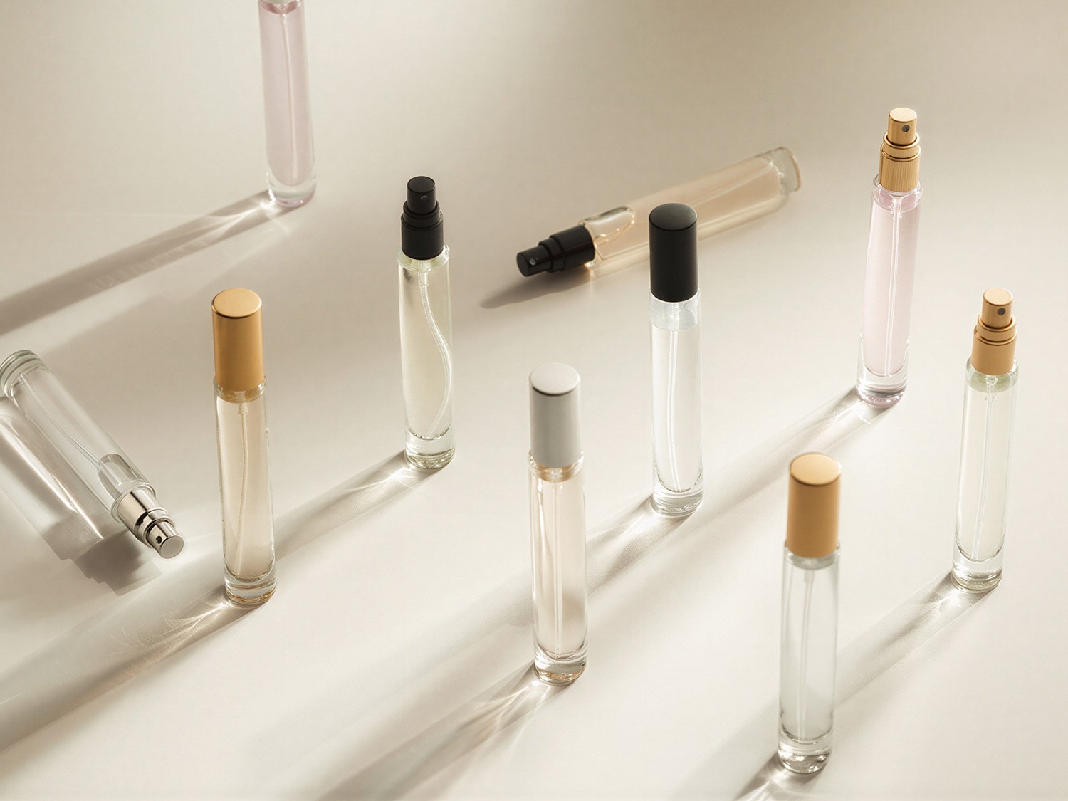 Eine Sammlung von durchsichtigen Parfümflaschen mit silbernen, goldenen und schwarzen Akzenten, die auf einer hellen Oberfläche angeordnet sind und ein elegantes und minimalistisches Erscheinungsbild bieten.