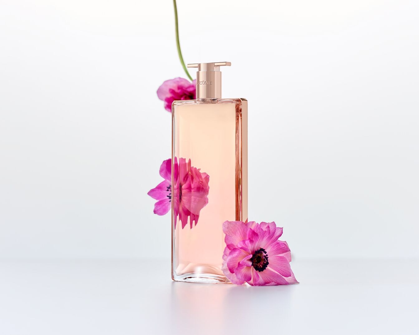 Stačiakampio formos rausvas „Lancome Idôle“ kūno losjonas su dozatoriumi, papuoštas trimis rožiniais žiedais.