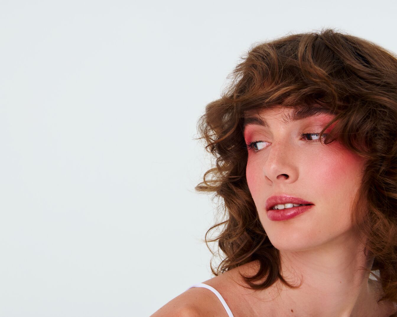Šviesiaplaukė moteris su rausvu akių šešėliu ir skaistalais, žiūrinti į kairę pusę.
