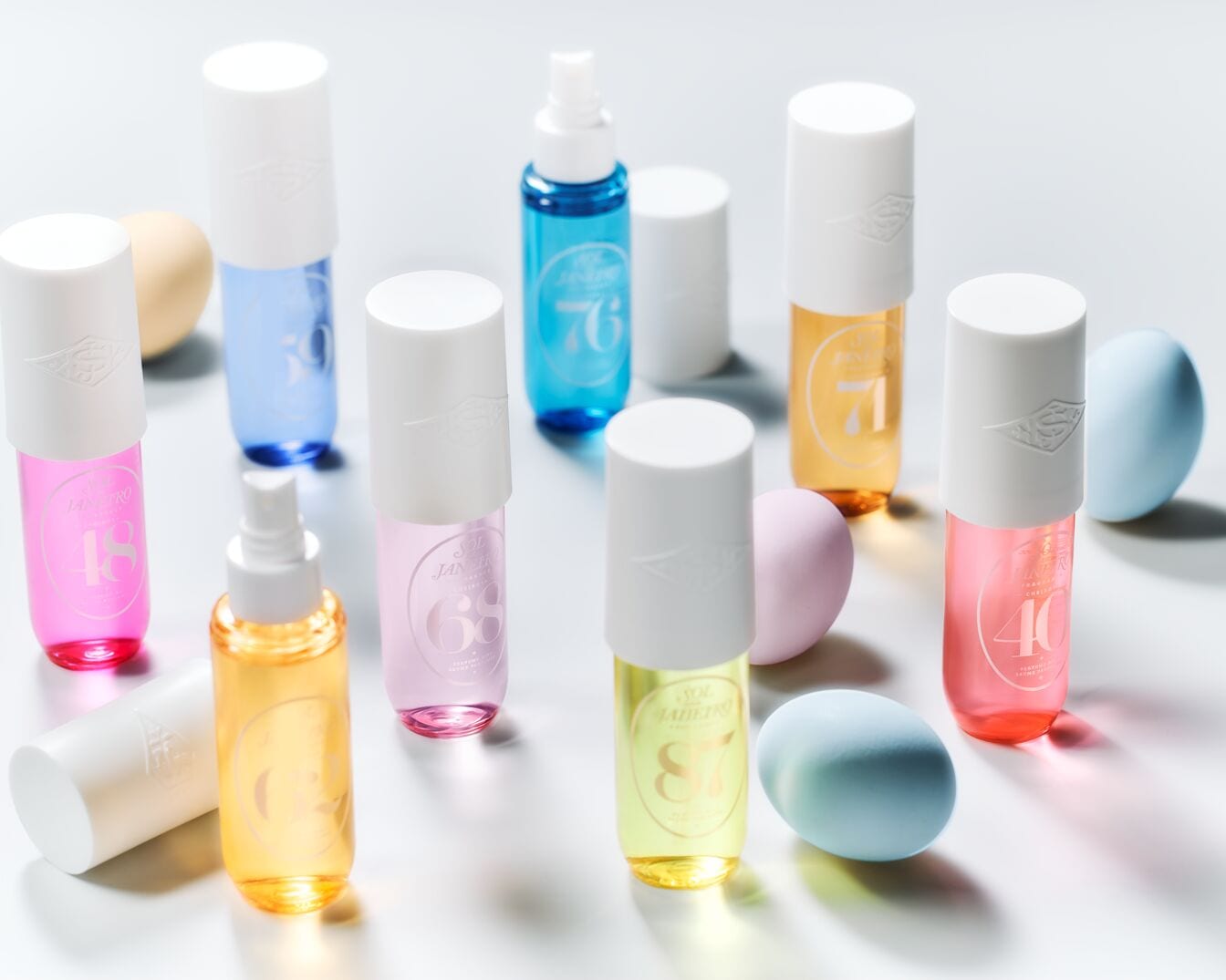 Spalvinga „Sol de Janeiro“ purškiklių kolekcija su baltais dangteliais ir pasteliniais kiaušiniais, sukuriančiais žaismingą ir patrauklią kompoziciją.