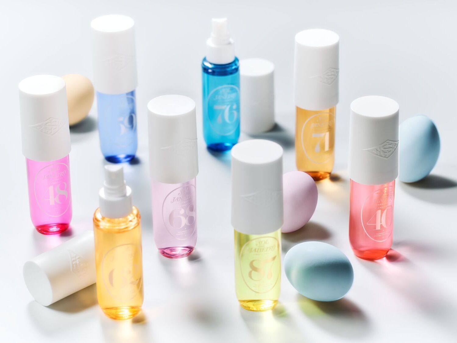 Įvairiaspalviai „Sol de Janeiro“ purškikliai su baltais dangteliais ir pasteliniais kiaušiniais sukuria žaismingą ir spalvingą kompoziciją.