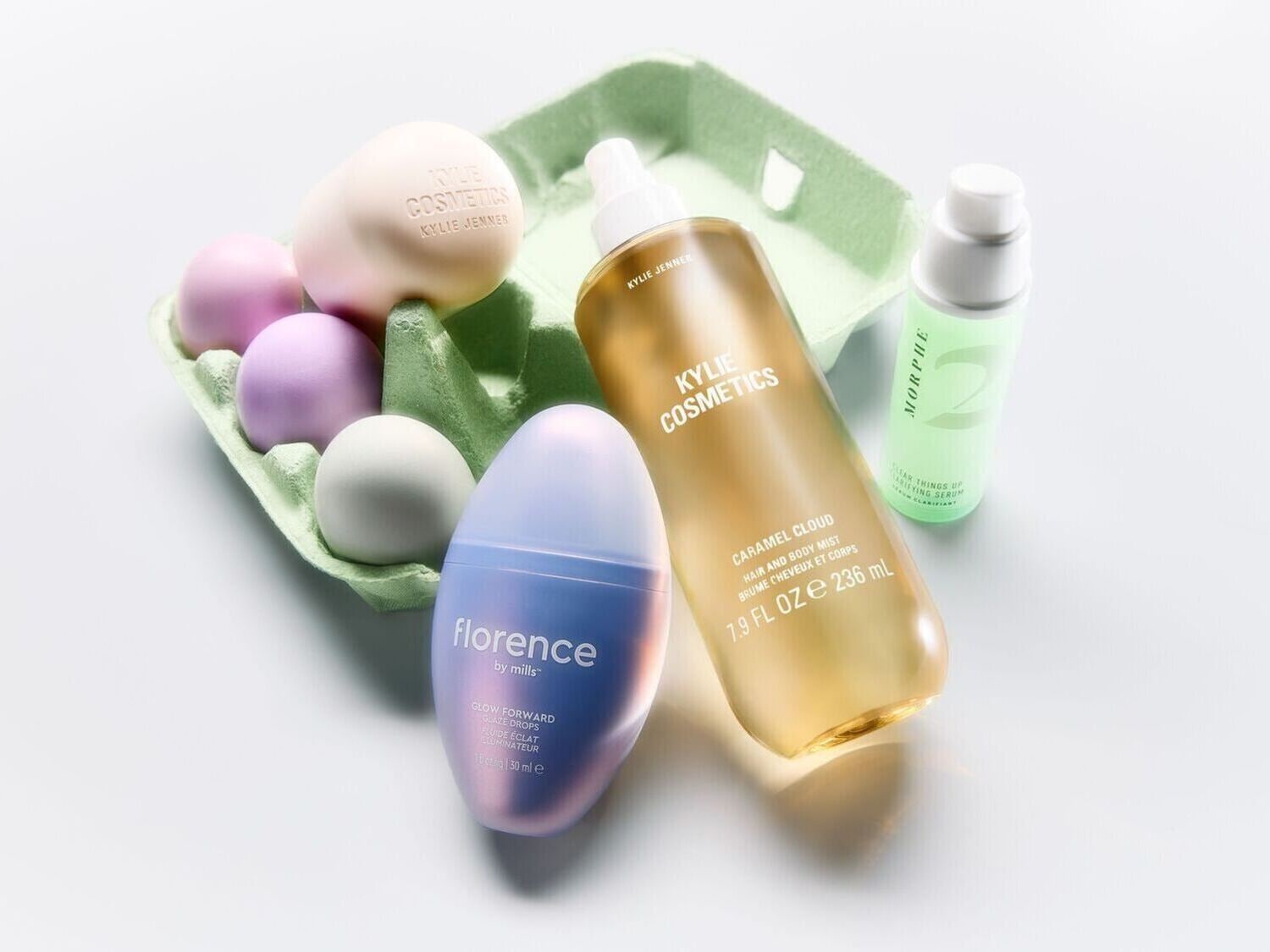 Kosmetikos rinkinys, įskaitant „Kylie Cosmetics“ ir „Florence by Mills“ produktus, išdėstytus šalia kiaušinių dėžutės su pasteliniais kiaušiniais, skirtas grožio produktų pristatymui.