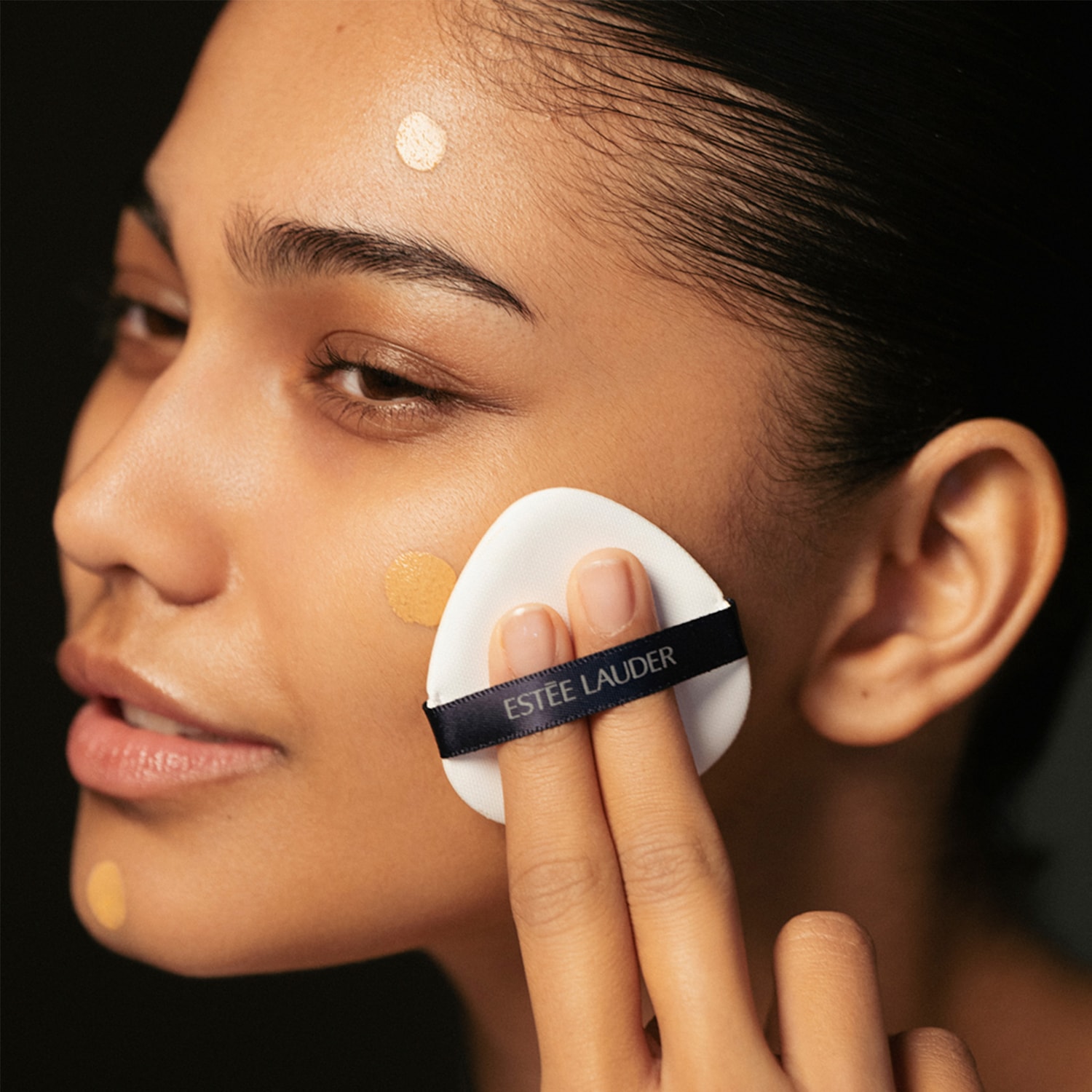 Nahaufnahme einer Frau, die mit einem Make-up-Schwämmchen von Estée Lauder Foundation auf ihr Gesicht aufträgt.