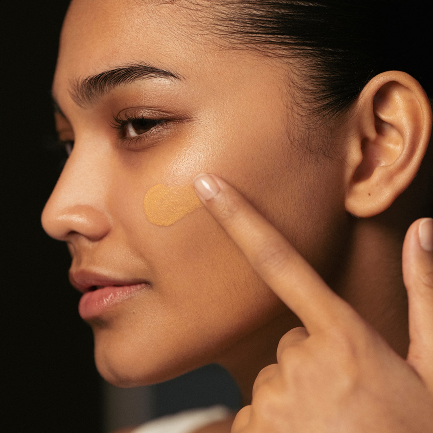 Nahaufnahme einer Frau, die mit dem Finger eine Foundation auf ihre Wange aufträgt, um den perfekten Farbton zu finden.