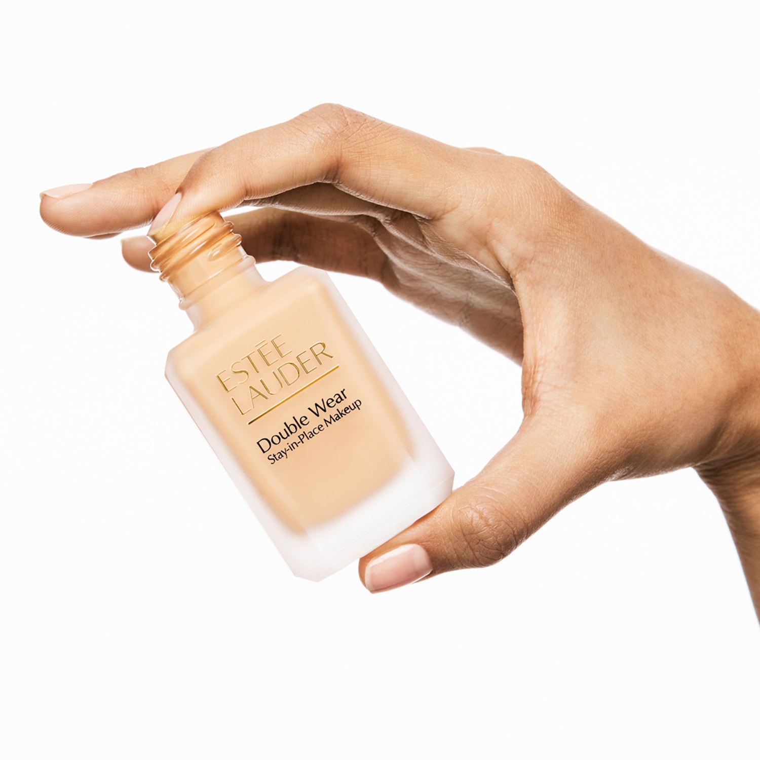 Eine Hand hält eine geöffnete Flasche Double Wear Stay-in-Place Makeup von  Estée Lauder vor weißem Hintergrund.