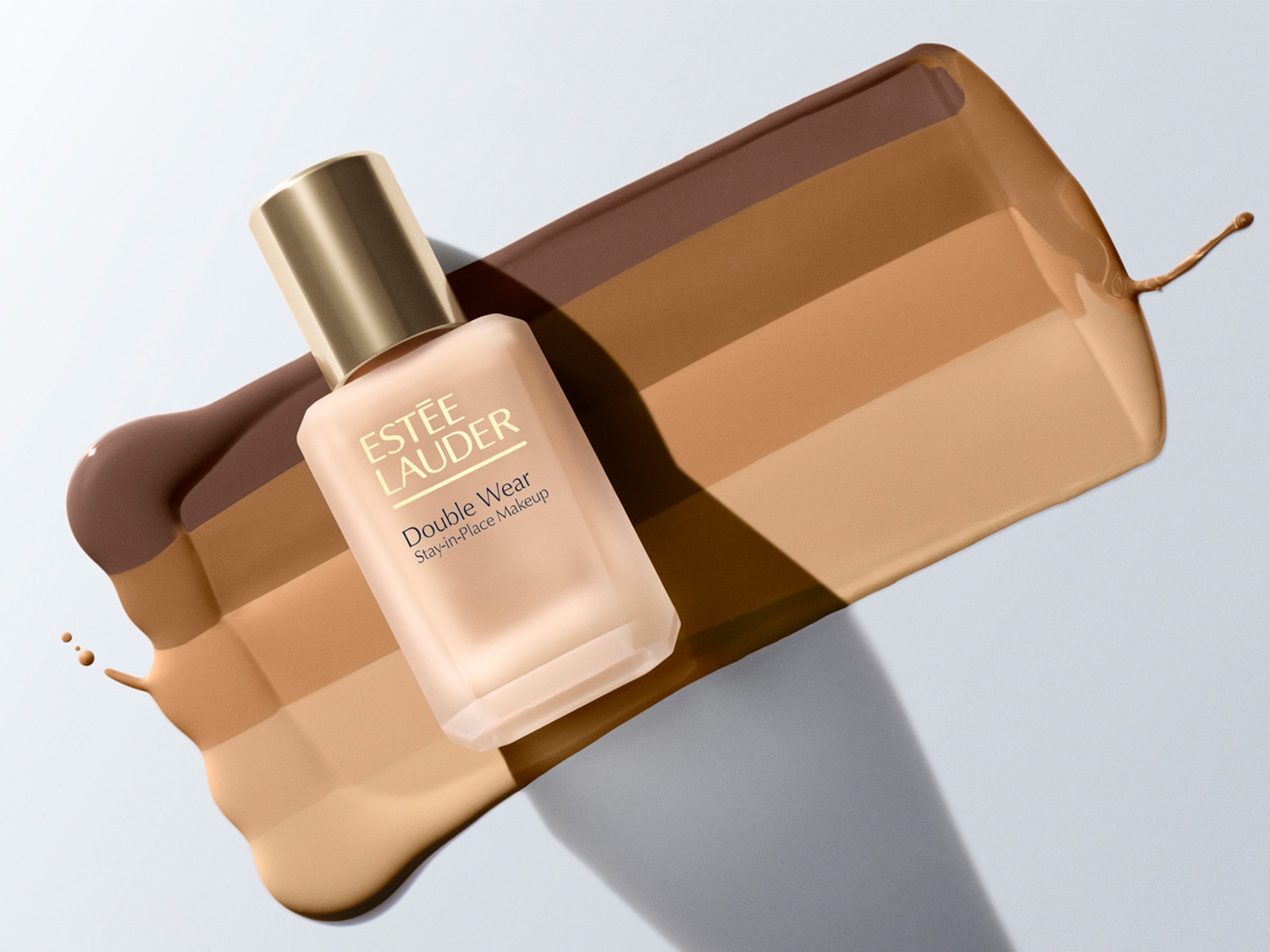 Das Double Wear Stay-in-Place Makeup von Estée Lauder in einer matten Glasflasche mit goldenem Deckel, umgeben von Farbtönen, die verschiedene Shades des Make-ups darstellen.