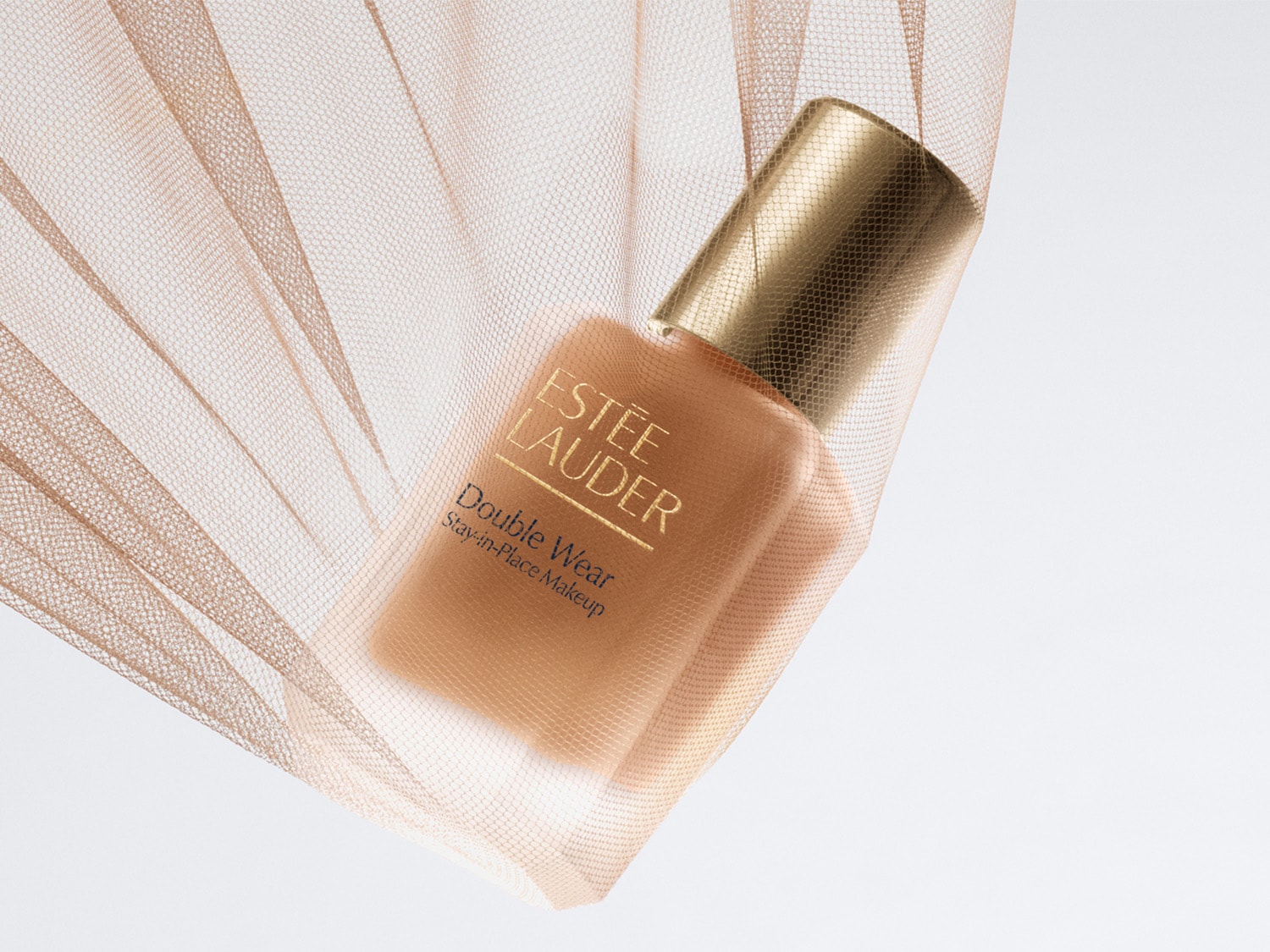 Das Double Wear Stay-in-Place Makeup von Estée Lauder in einer matten Glasflasche mit goldenem Deckel, umhüllt von zartem, beigefarbenem Tüll.