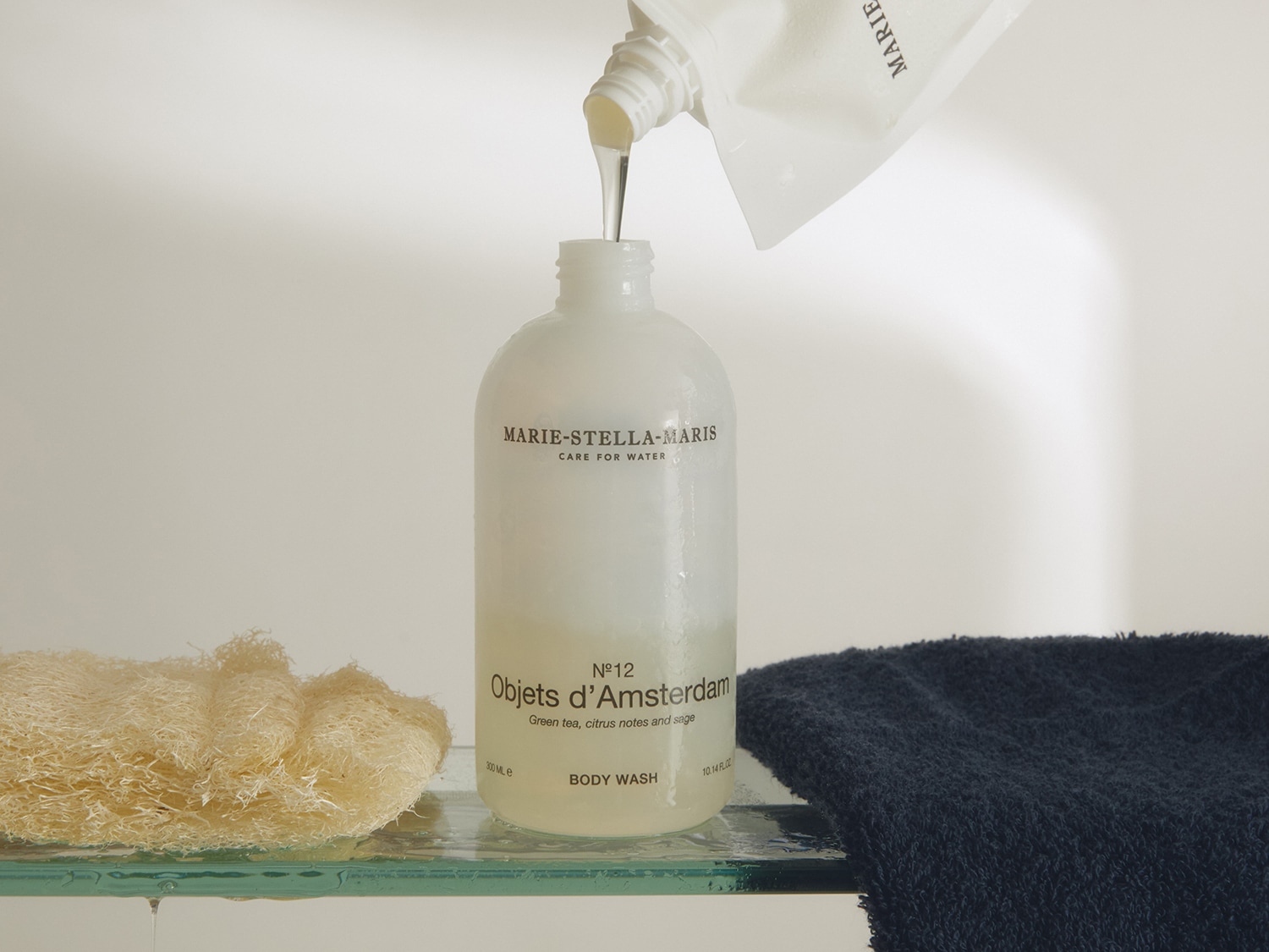 Le flacon blanc de gel douche Marie-Stella-Maris Objets d'Amsterdam N°12, infusé de thé vert, d'agrumes et de sauge, est rechargé à partir d'un sachet de recharge blanc.