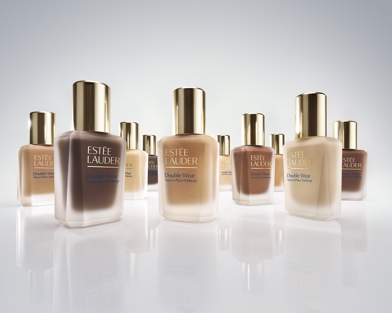 Découvrez le fond de teint Double Wear Stay-in-Place d'Estée Lauder, présenté dans des flacons en verre aux teintes variées, avec des bouchons dorés.