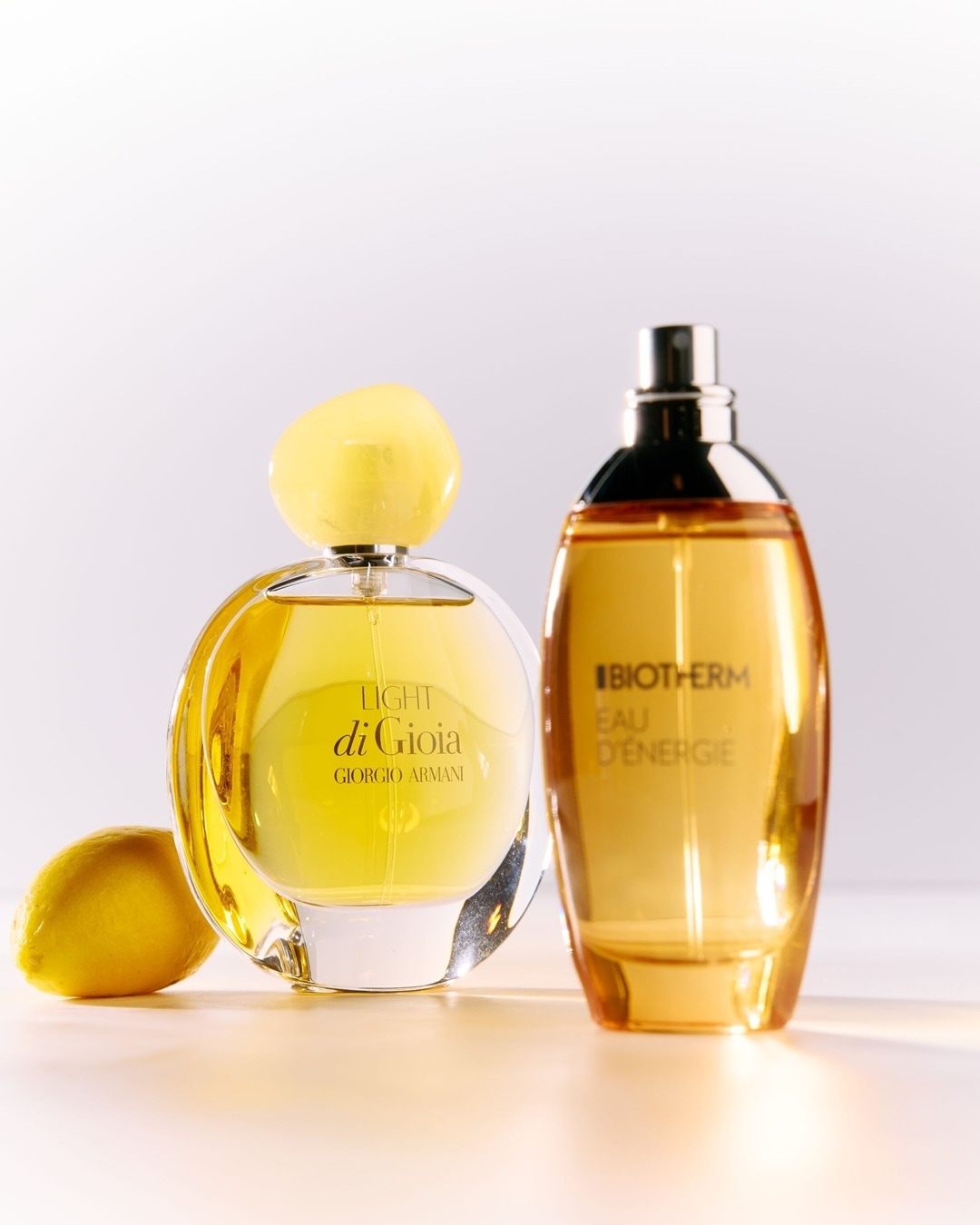 Deux parfums aux teintes dorées, l'un de Giorgio Armani et l'autre de Biotherm, évoquant des notes fraîches et énergisantes, accompagnés d'un citron jaune vif.