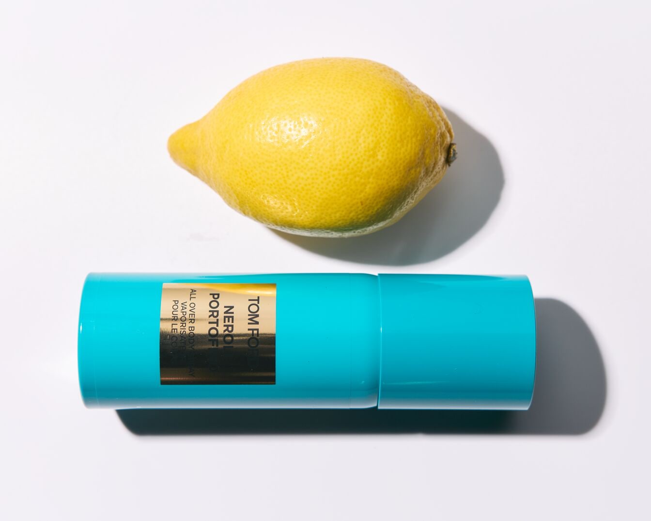 Un citron jaune vif repose à côté d'un flacon turquoise de Tom Ford Neroli Portofino, évoquant un parfum frais et estival.