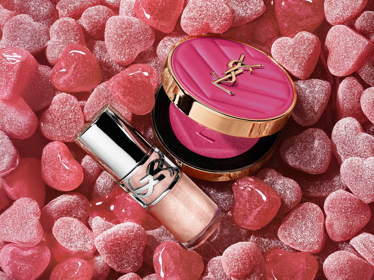 Rosa Süßigkeitenherzen umgeben einen YSL-Highlighter mit silberner Kappe und einen rosa Rouge mit goldenem Rand.