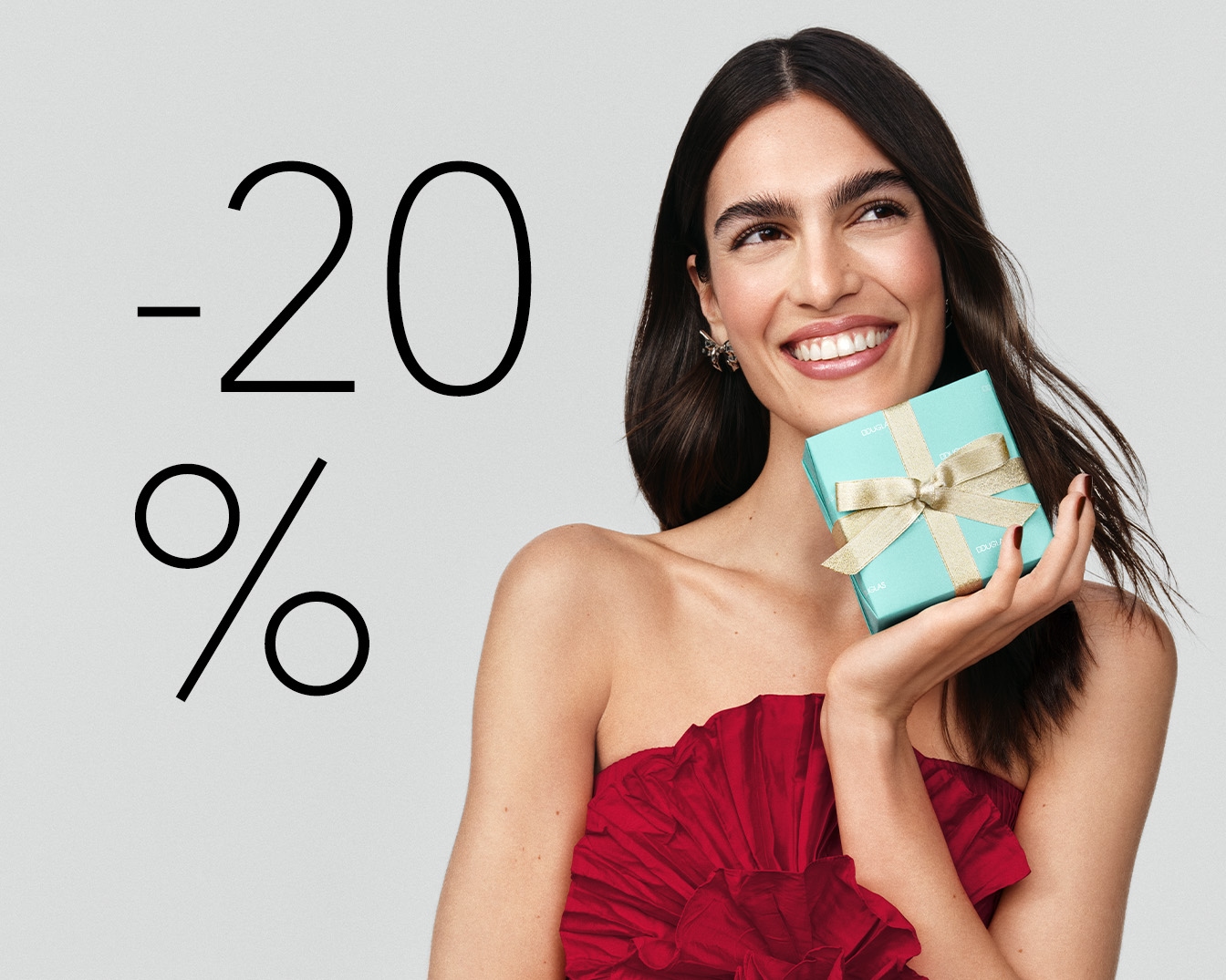 Uśmiechnięta kobieta w czerwonej sukience trzymająca w dłoni turkusowe pudełko z kokardą na tle napisu -20%.