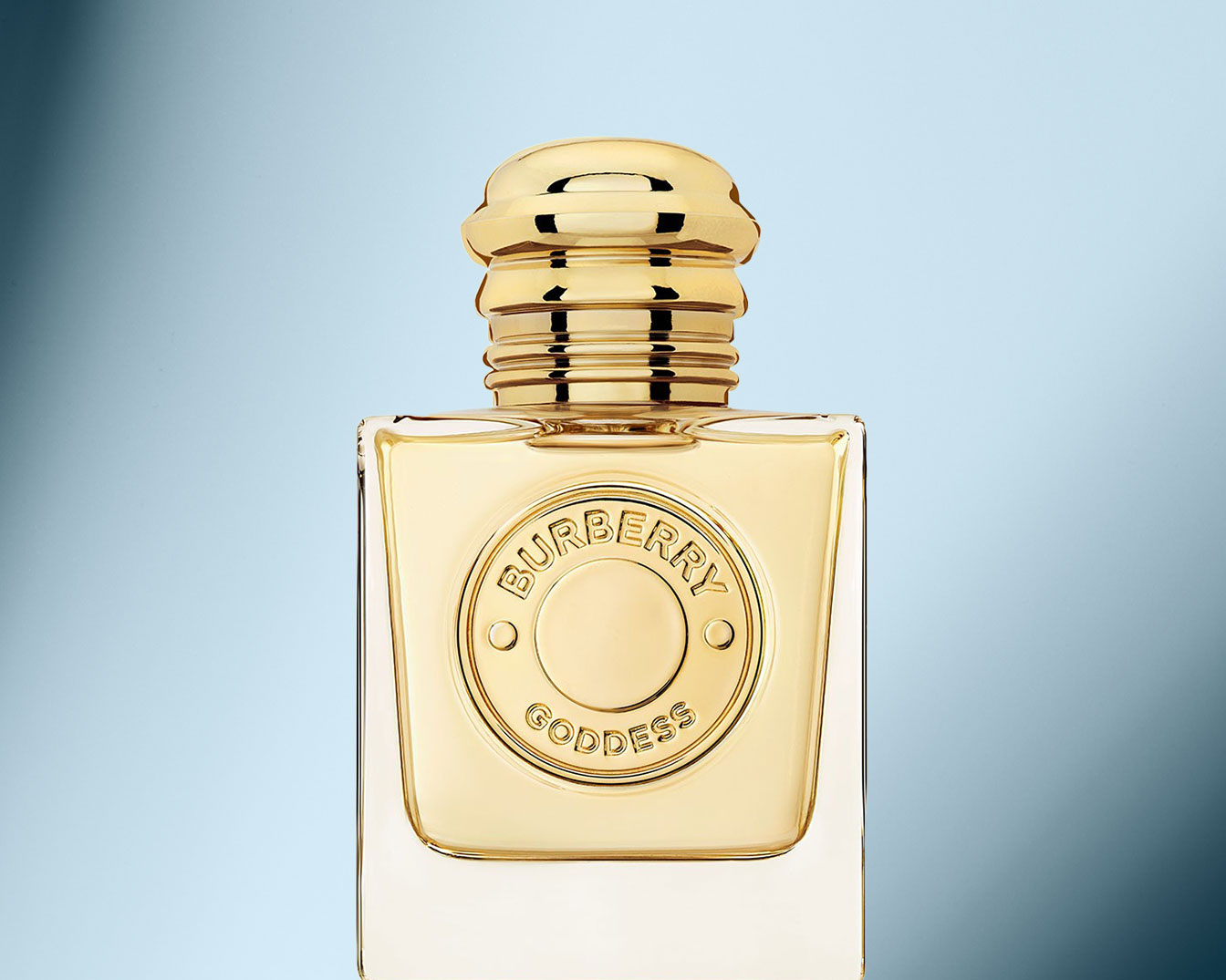 Goldener Burberry Göttin Parfümflakon mit quadratischer Form und glänzendem Verschluss vor hellblauem Hintergrund.