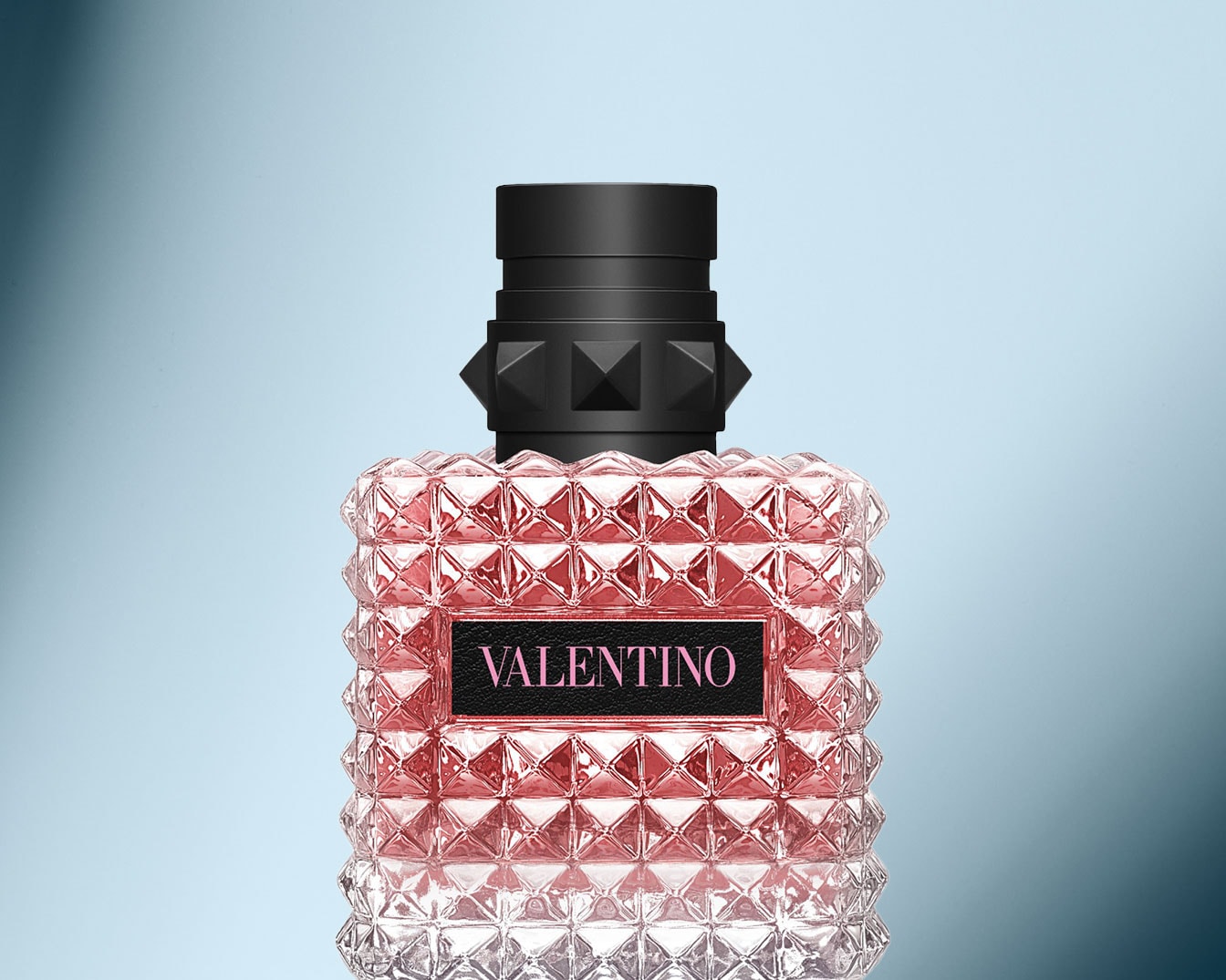 Nahaufnahme eines VALENTINO Parfums mit einem rosa getönten, facettierten Glasflakon und einem schwarzen Verschluss mit pyramidenförmigen Nieten.