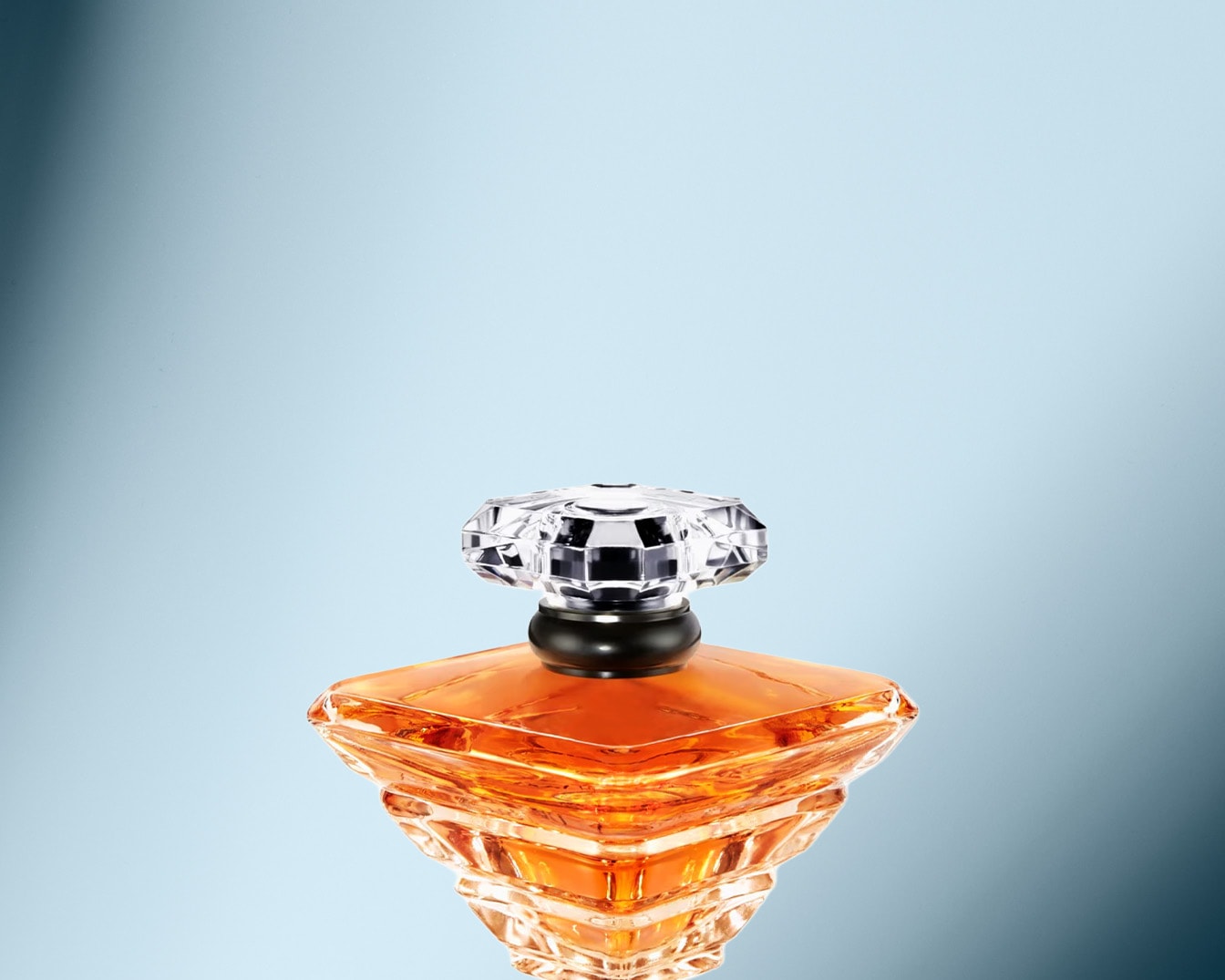 Nahaufnahme eines quadratischen Parfümflakons mit bernsteinfarbenem Inhalt und einem facettierten, klaren Verschluss auf hellblauem Hintergrund.
