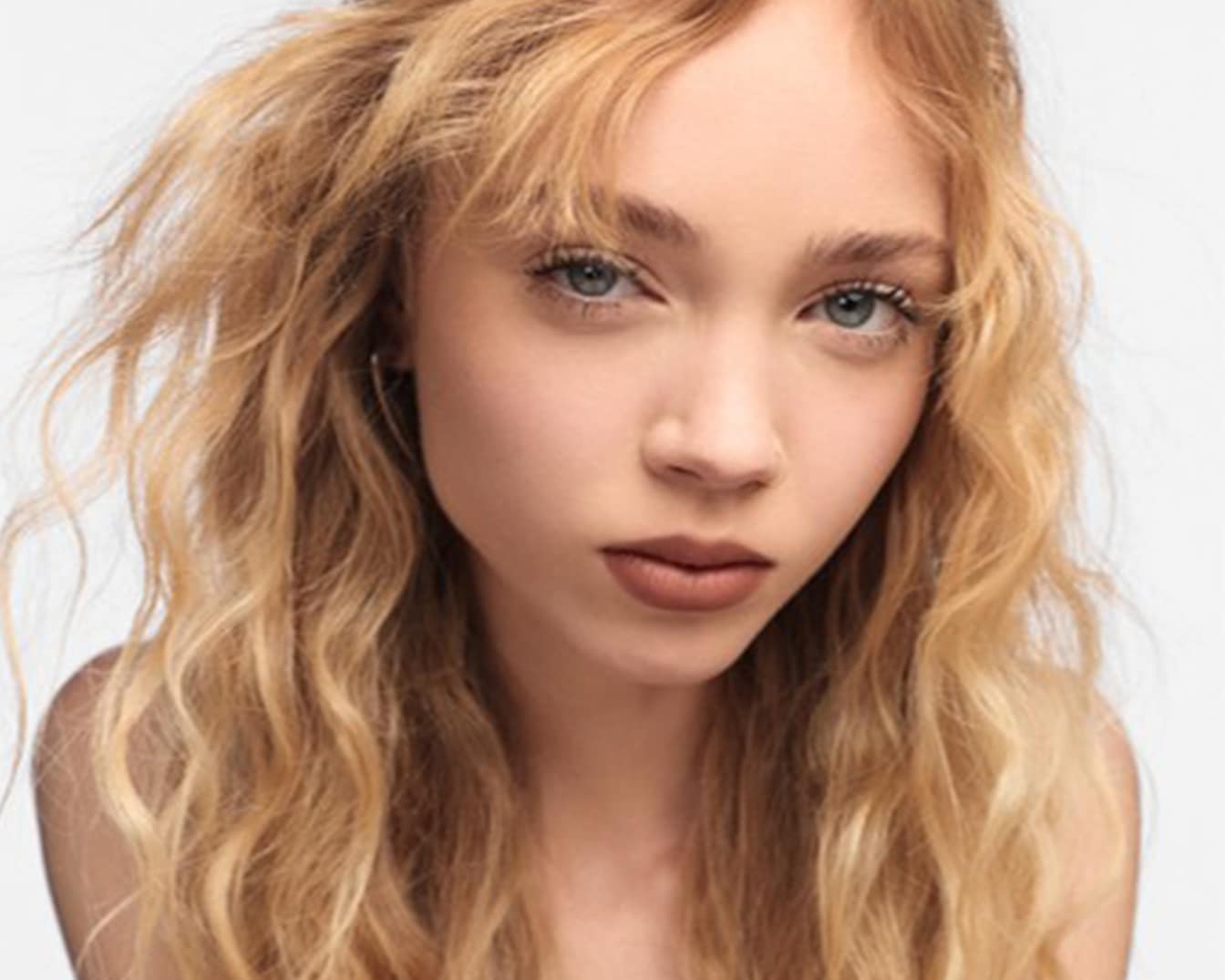 Primo piano di una modella con lunghi capelli biondi ondulati e labbra marroni, che mette in risalto la sua bellezza naturale.