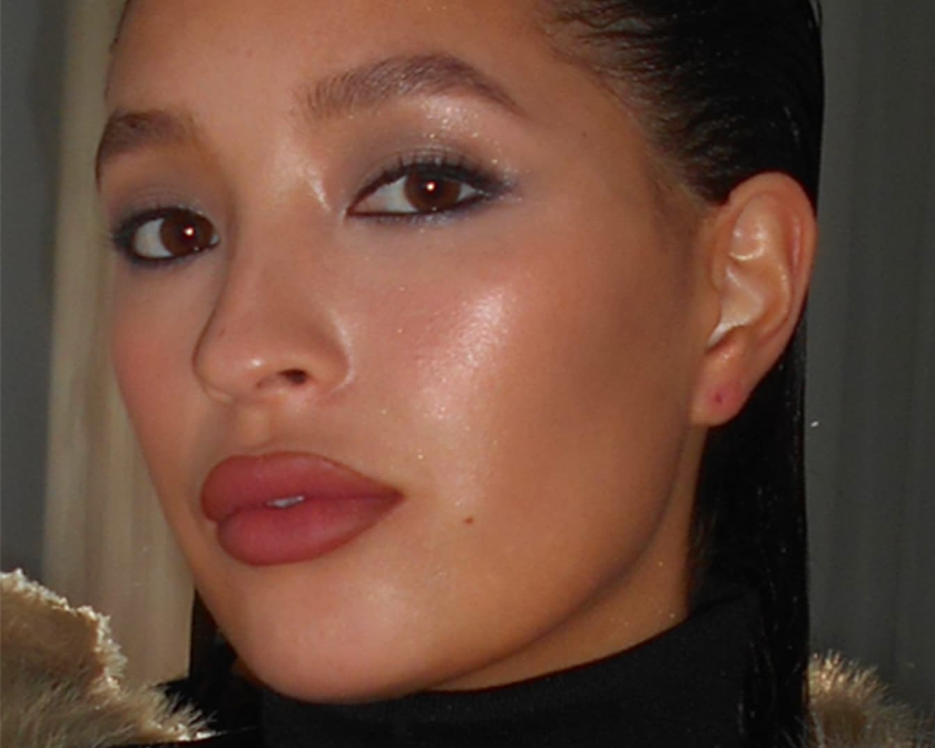 Primo piano di una modella con occhi marroni, ombretto scintillante, labbra rosa opaco e pelle luminosa.