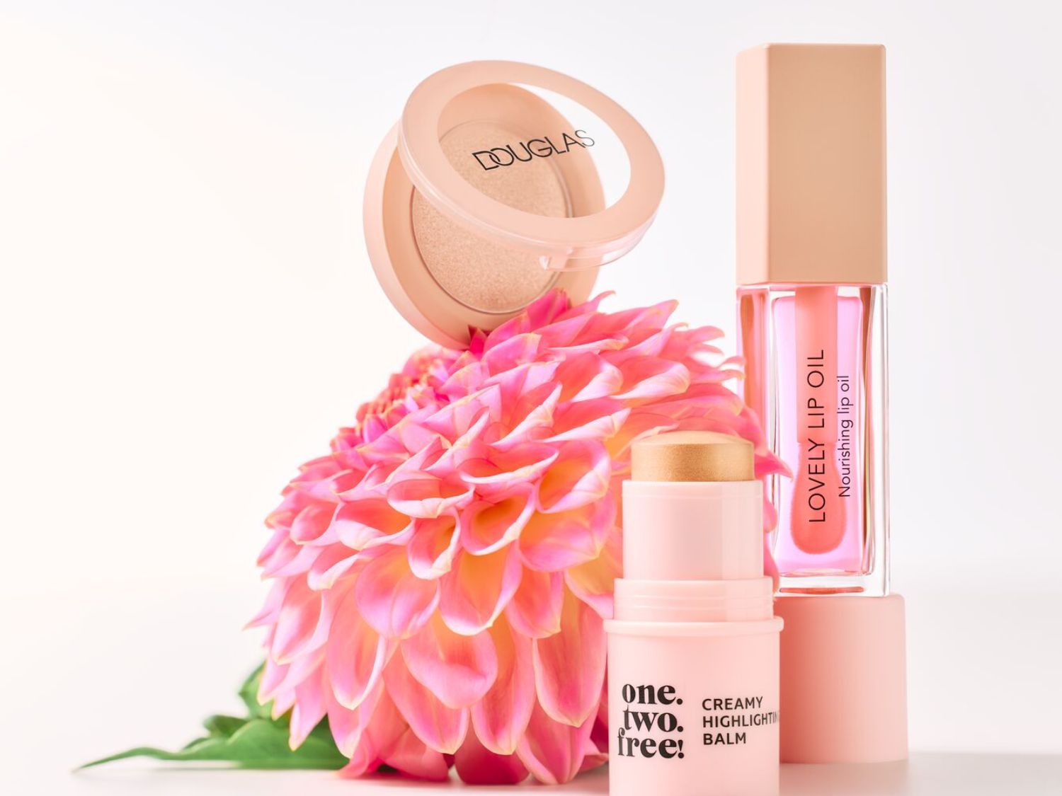 Douglas make-up set met een blush, een highlighter balm en een lipolie in zachte, roze tinten, gepresenteerd met een roze bloem.