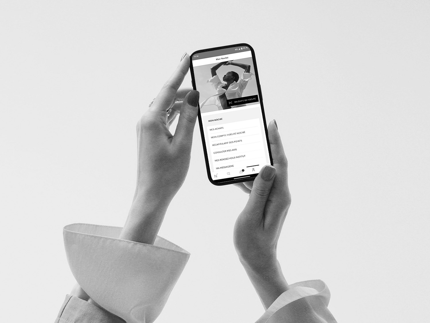 Gros plan sur un smartphone tenu par une main, affichant l'application Nocibé avec les options Mon Nocibé, Mes Achats, Mon Compte Fidélité Nocibé, et plus.