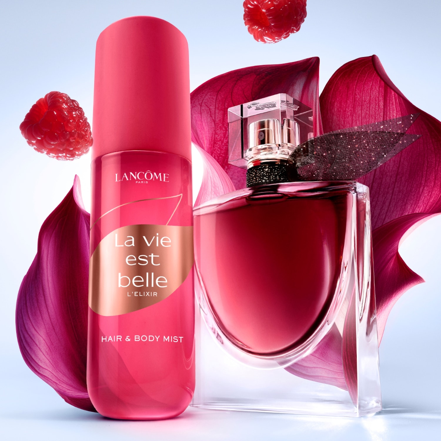 La Vie Est Belle L'Elixir Hair & Body Mist von Lancôme in einer pinkfarbenen Flasche neben dem La Vie Est Belle L'Elixir Parfüm, umgeben von Himbeeren und Blütenblättern.