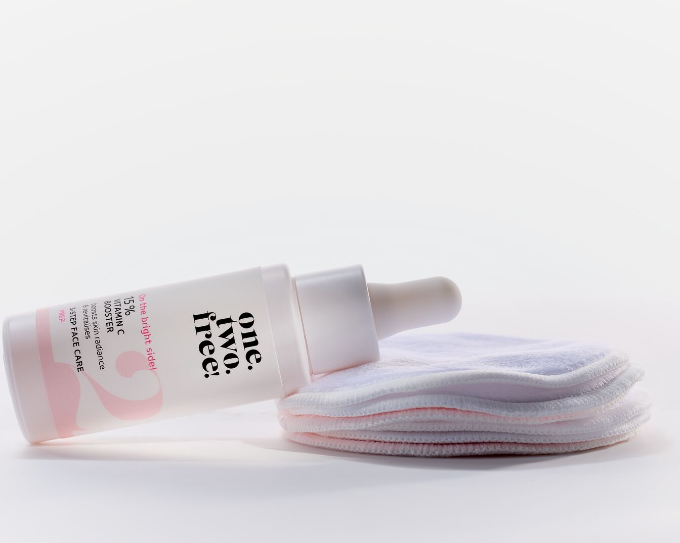Flacon blanc de sérum One.Two.Free! avec 15% de vitamine C, promettant d'illuminer et de revitaliser la peau, accompagné de disques démaquillants réutilisables.
